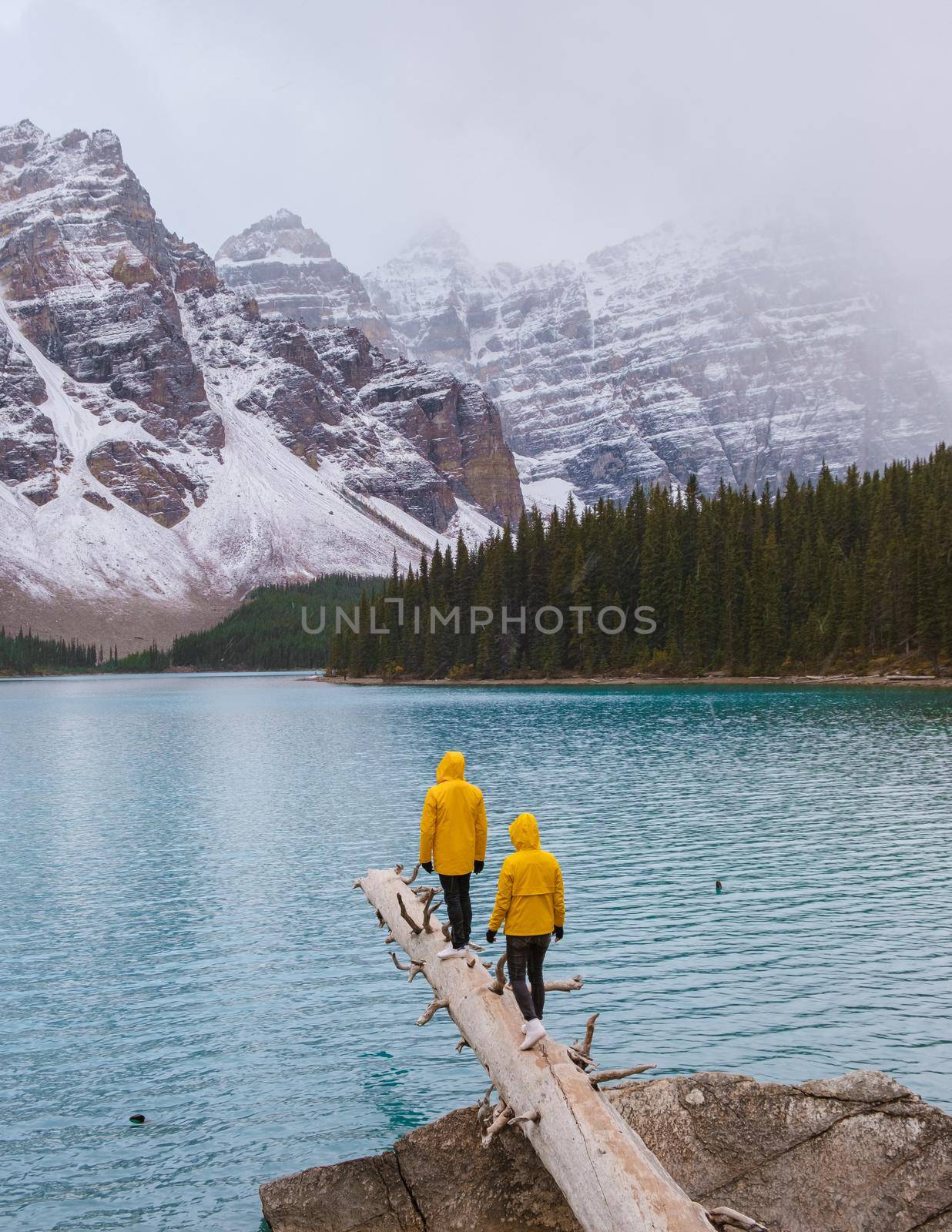 Lake moraine during a cold snowy day in Autumn in Canada, Beautiful turquoise waters of the Moraine lake with snow. couple of men and women in yellow raincoat jacket during snow