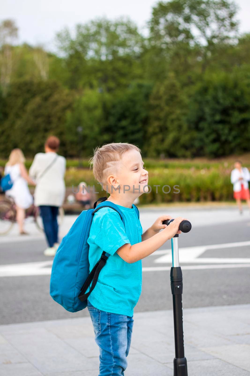 A boy on a scooter along the embankment of the city. Journey. Backpack on the back. The face expresses natural joyful emotions. Not staged photos from life.