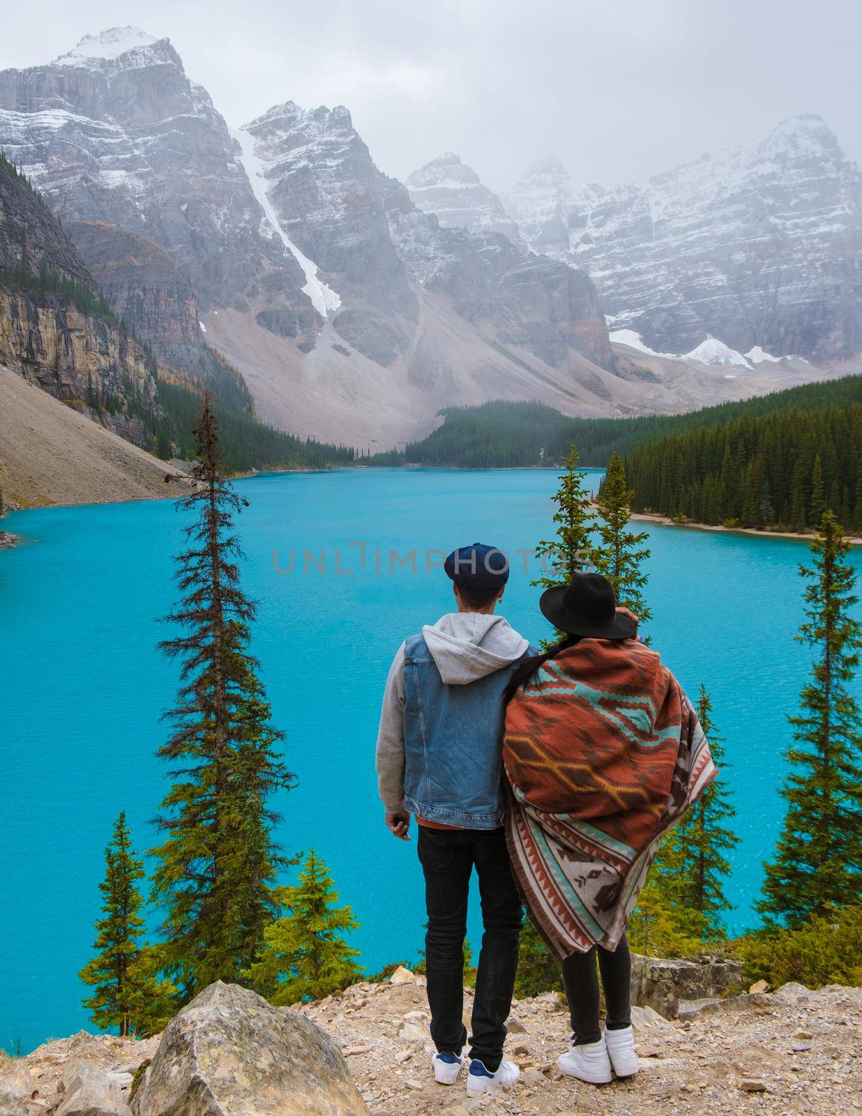 Lake moraine during a cold snowy day in Canada, turquoise waters of the Moraine lake with snow. Banff National Park of Canada Canadian Rockies. Young couple men and women standing by the lake