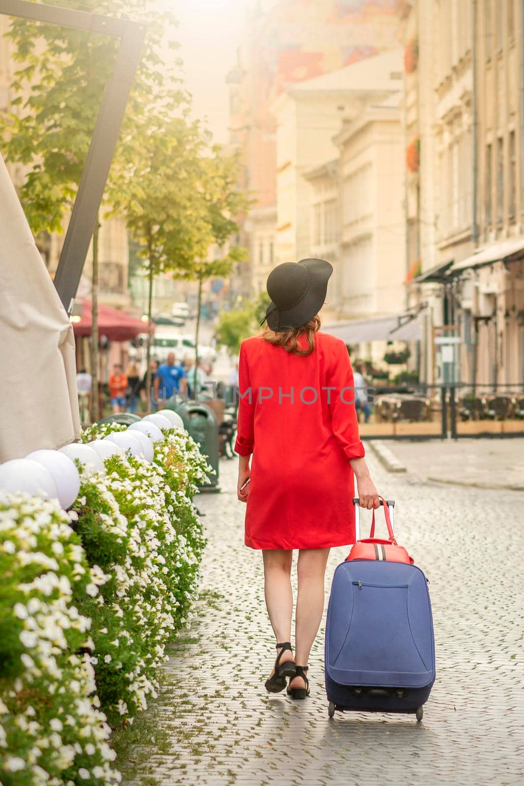 A young woman in a black hat with a suitcase walks on the European city street