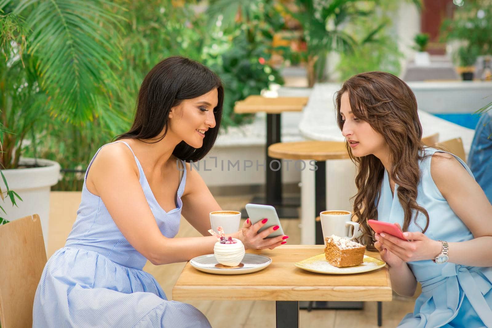 Two beautiful young women together watching something on the phone at the table in a cafe