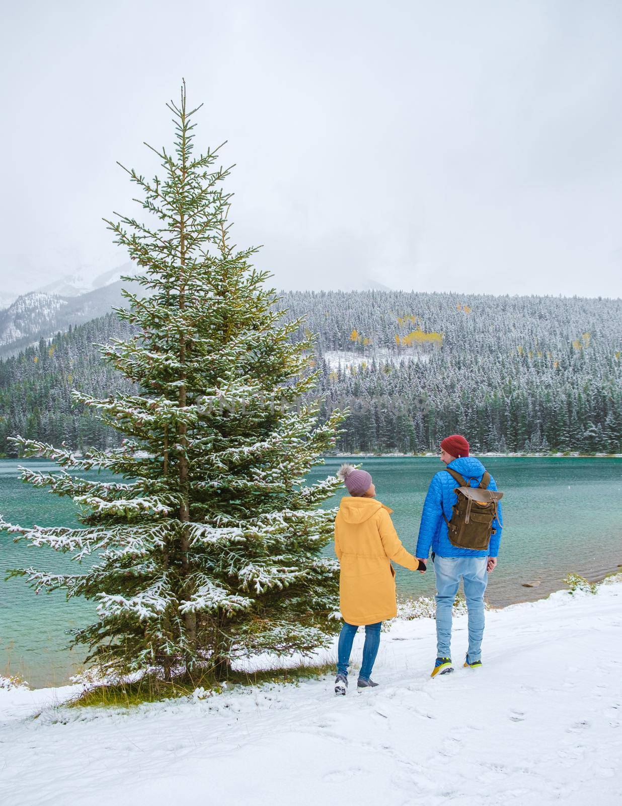 Minnewanka lake in the Canadian Rockies in Banff Alberta Canada with turquoise water, Lake Two Jack in the Rocky Mountains of Canada. a couple of men and women hiking by the lake during snow weather