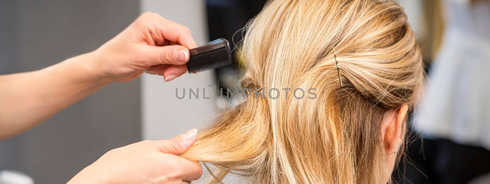 Rear View of a hairdresser combs blonde hair of the young woman in a beauty salon
