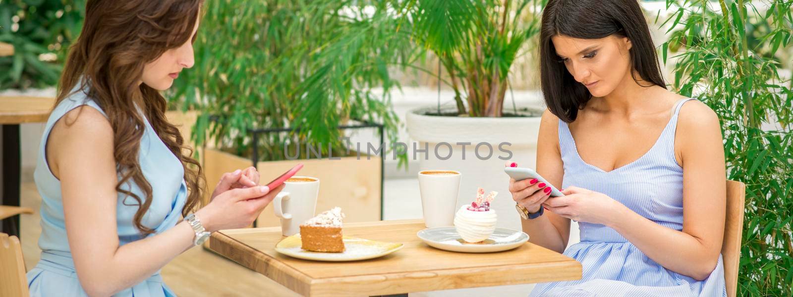 Two young women looking their smartphones while sitting in a cafe. Technology people addictions