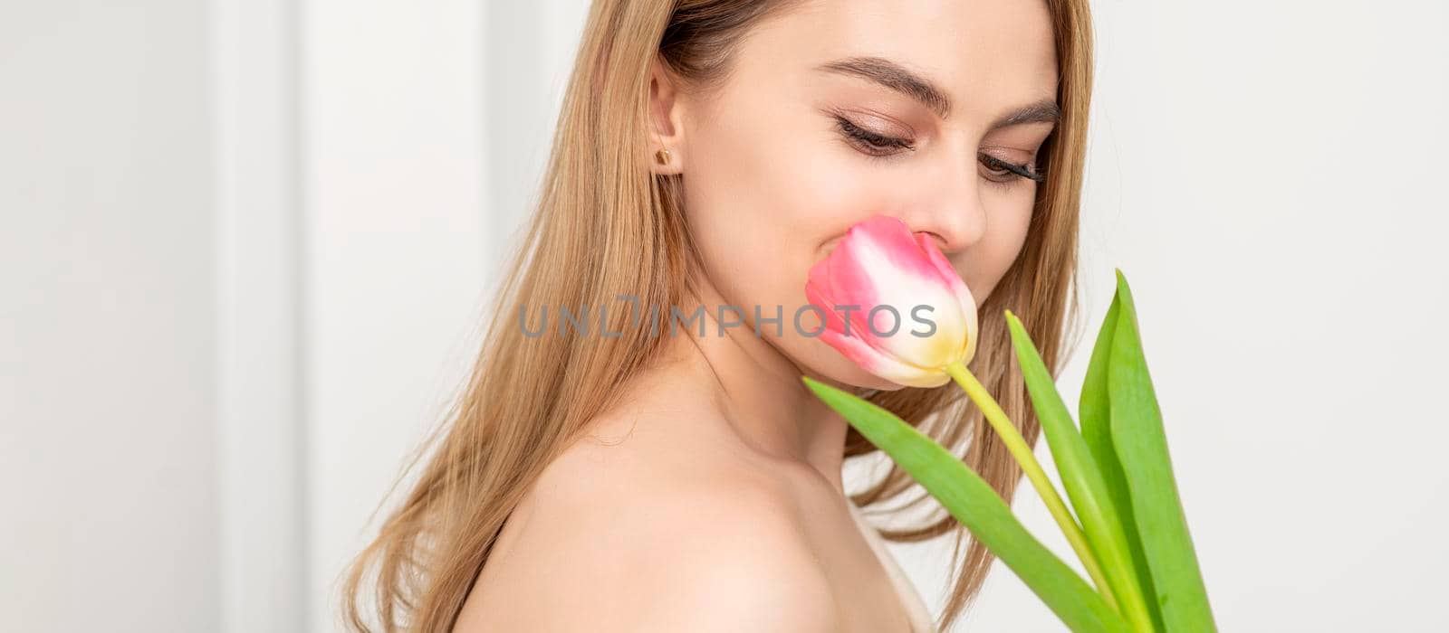 Beautiful caucasian young woman with one tulip looking on a flower against a white background