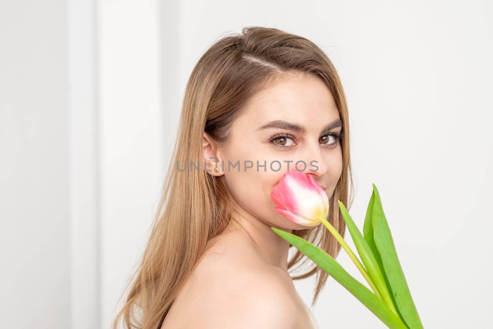 Beautiful caucasian young woman with one tulip against a white background