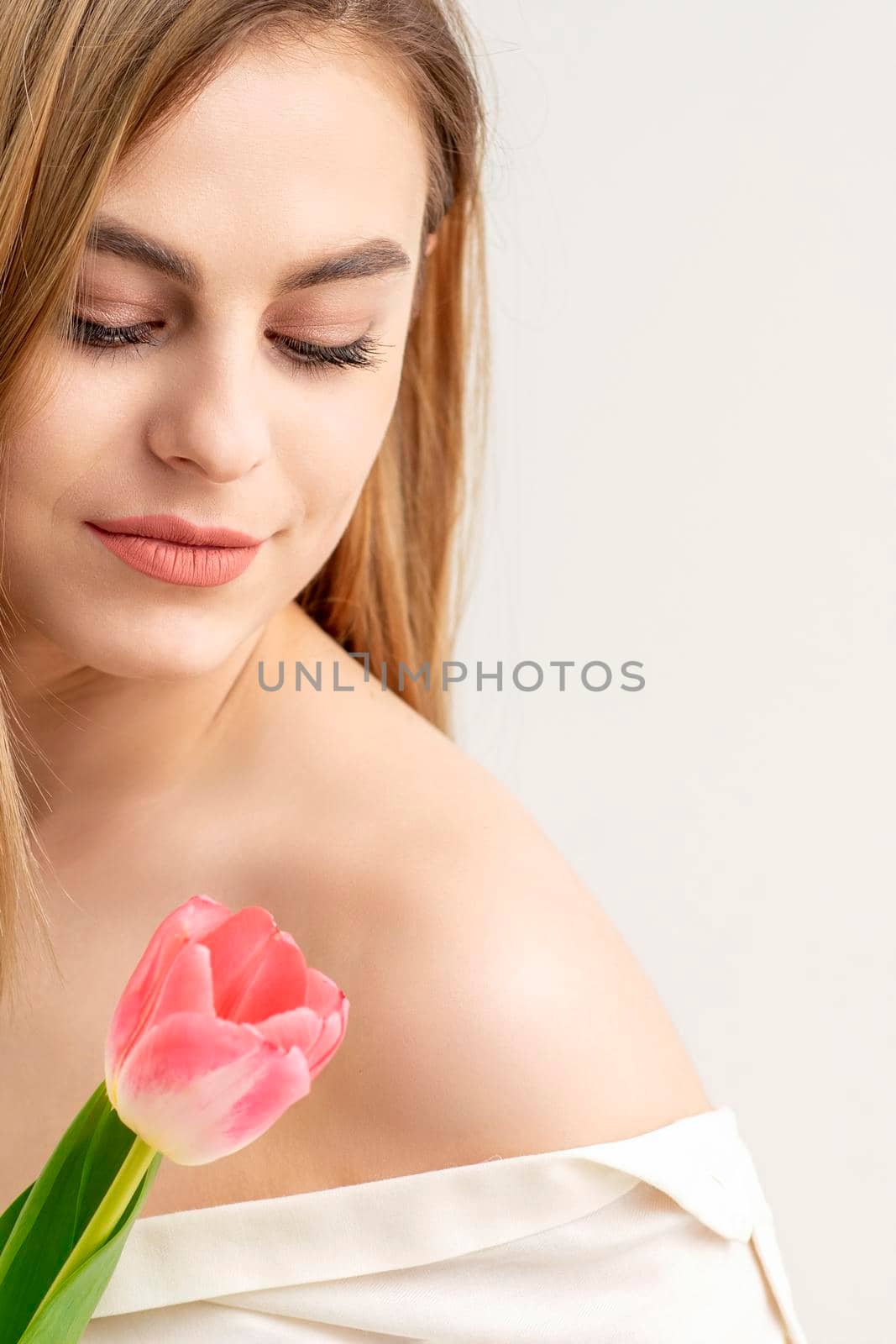 Beautiful caucasian young woman with one tulip looking on a flower against a white background