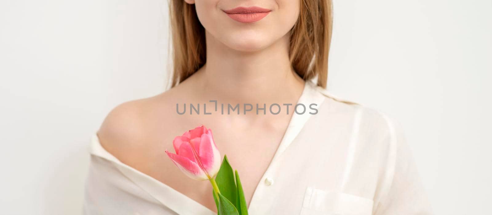 Half face of a beautiful caucasian young woman with one tulip against a white background