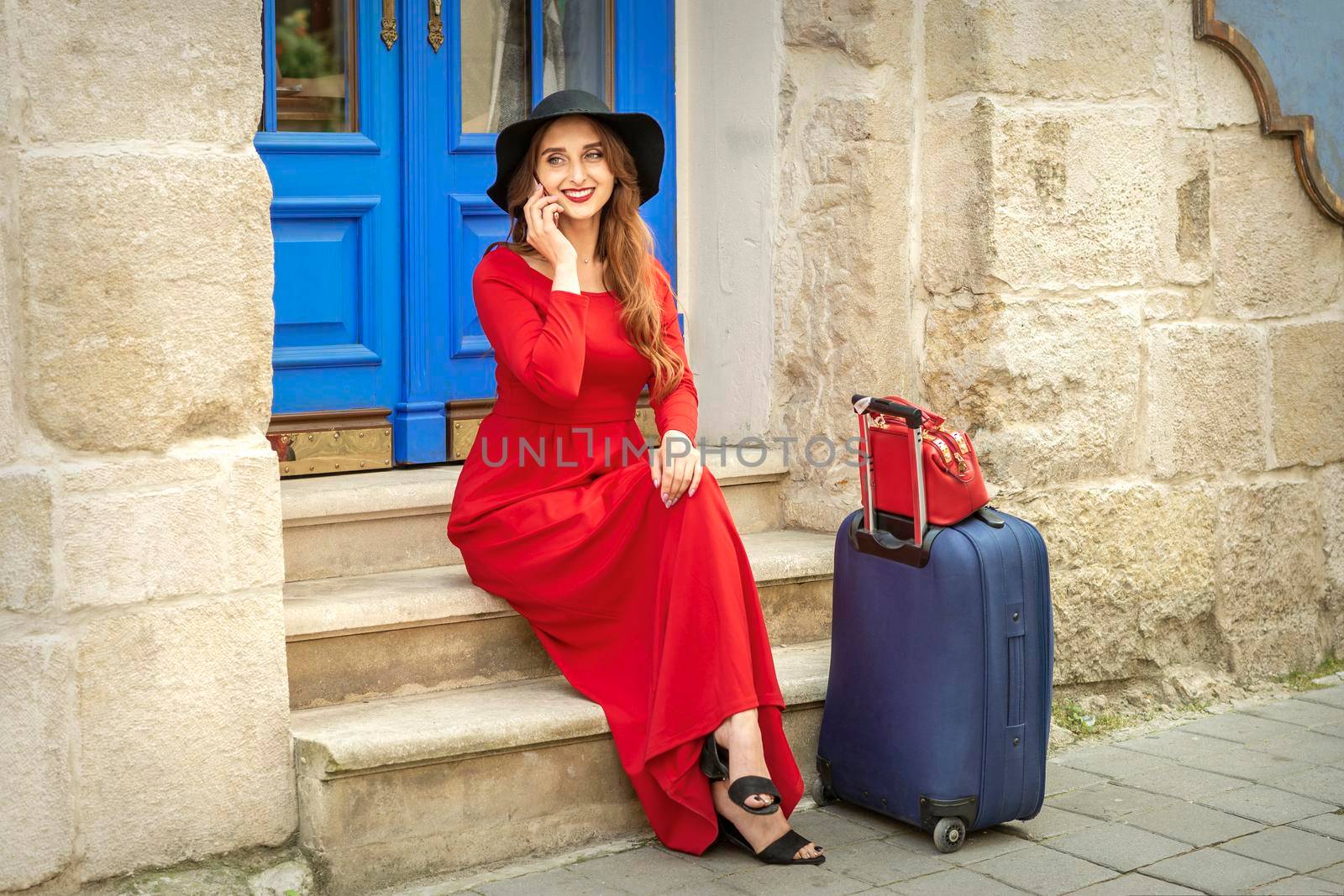 Beautiful young caucasian tourist woman talks on the phone sitting on the stairs at the door on the street