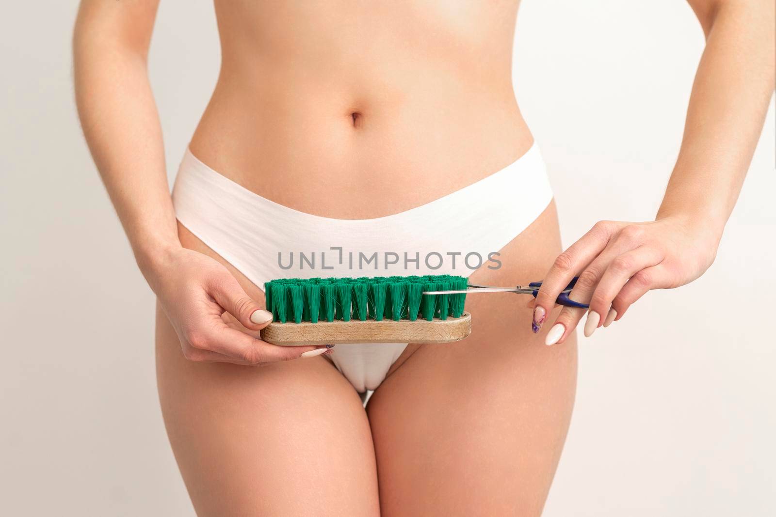 Epilation concept. A young caucasian woman wears white panties is cutting a cleaning brush with scissors standing on white background