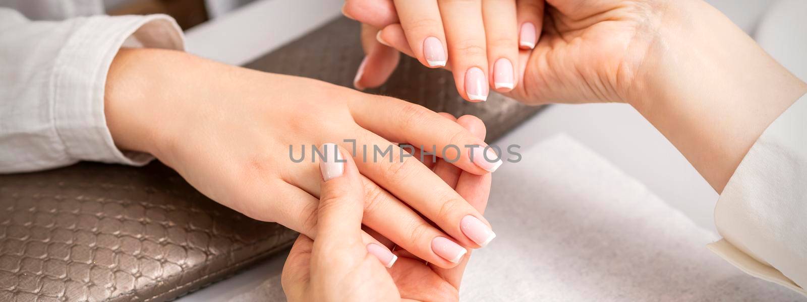 Manicure master holds hands of a young woman showing finished manicure on fingers in a nail salon