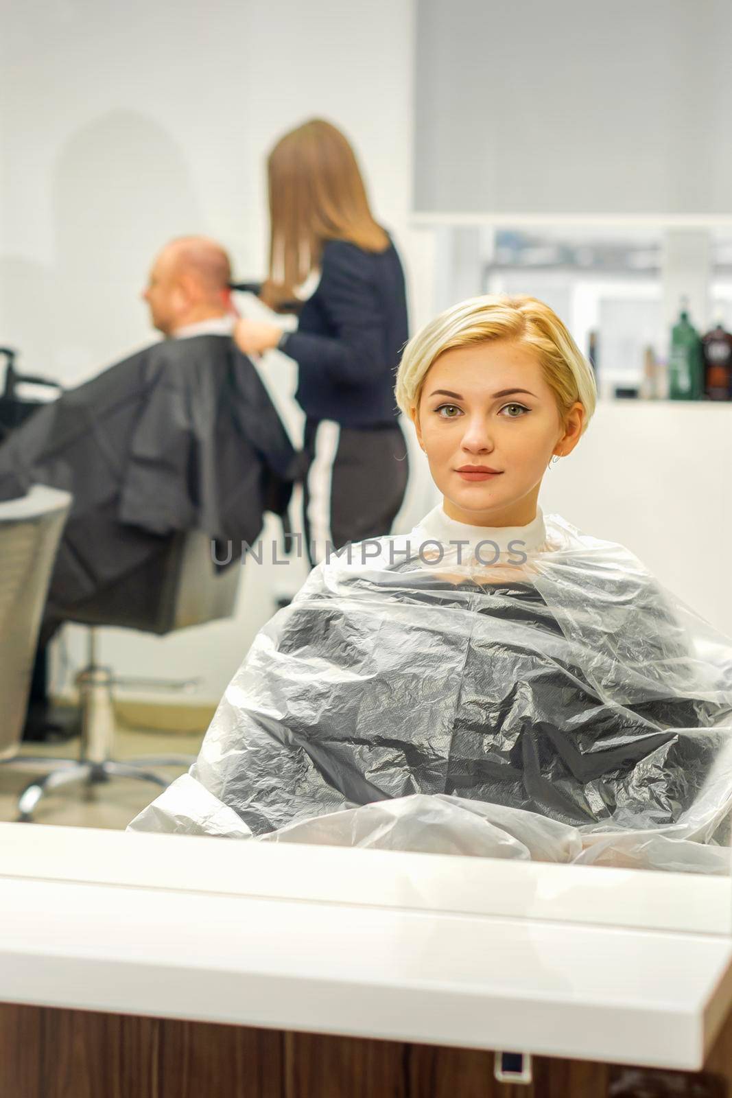 Young female client waiting for the hairdresser looking in the mirror in a hair salon