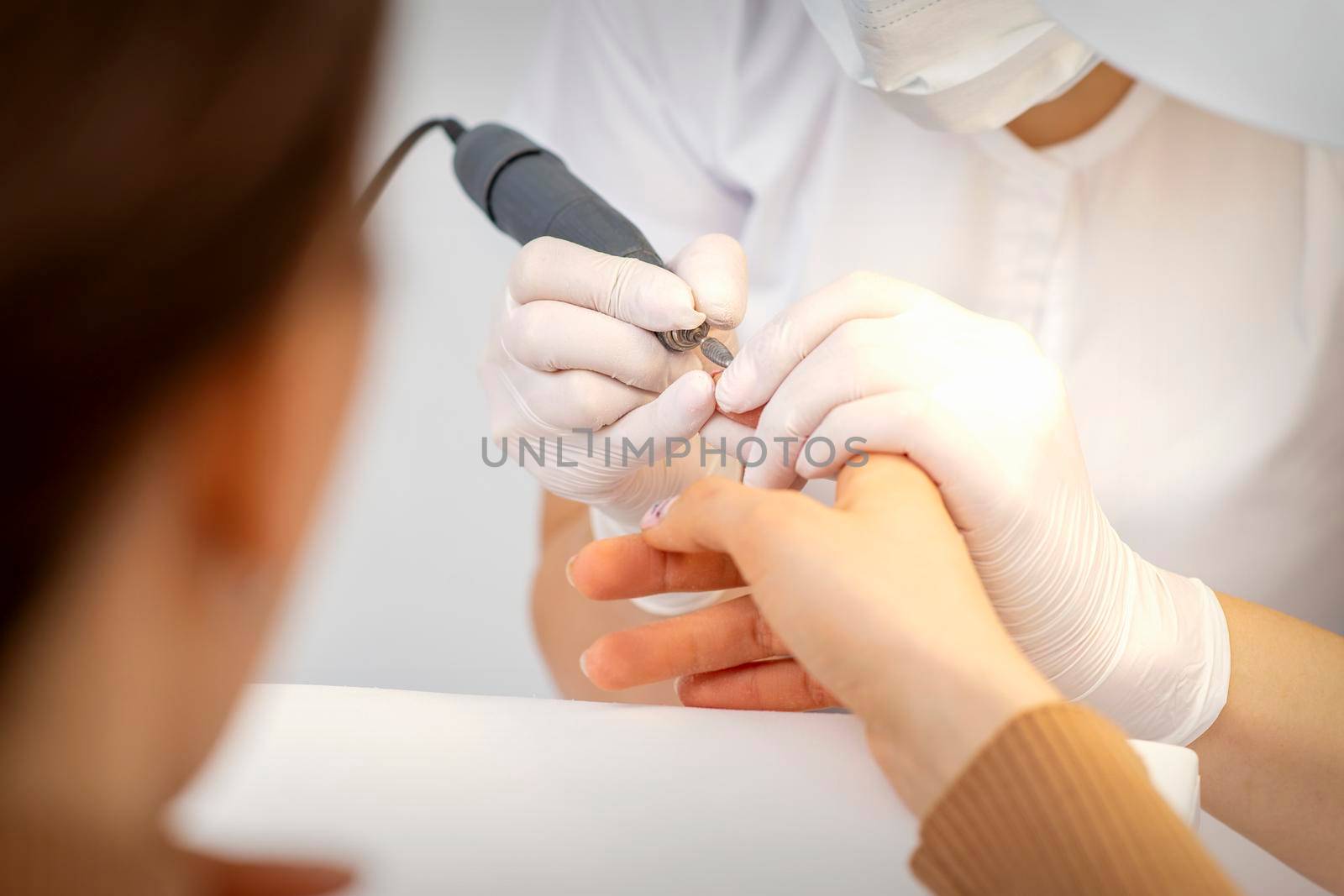 Closeup of manicure master removes nail polish uses an electric nail file in a nail salon