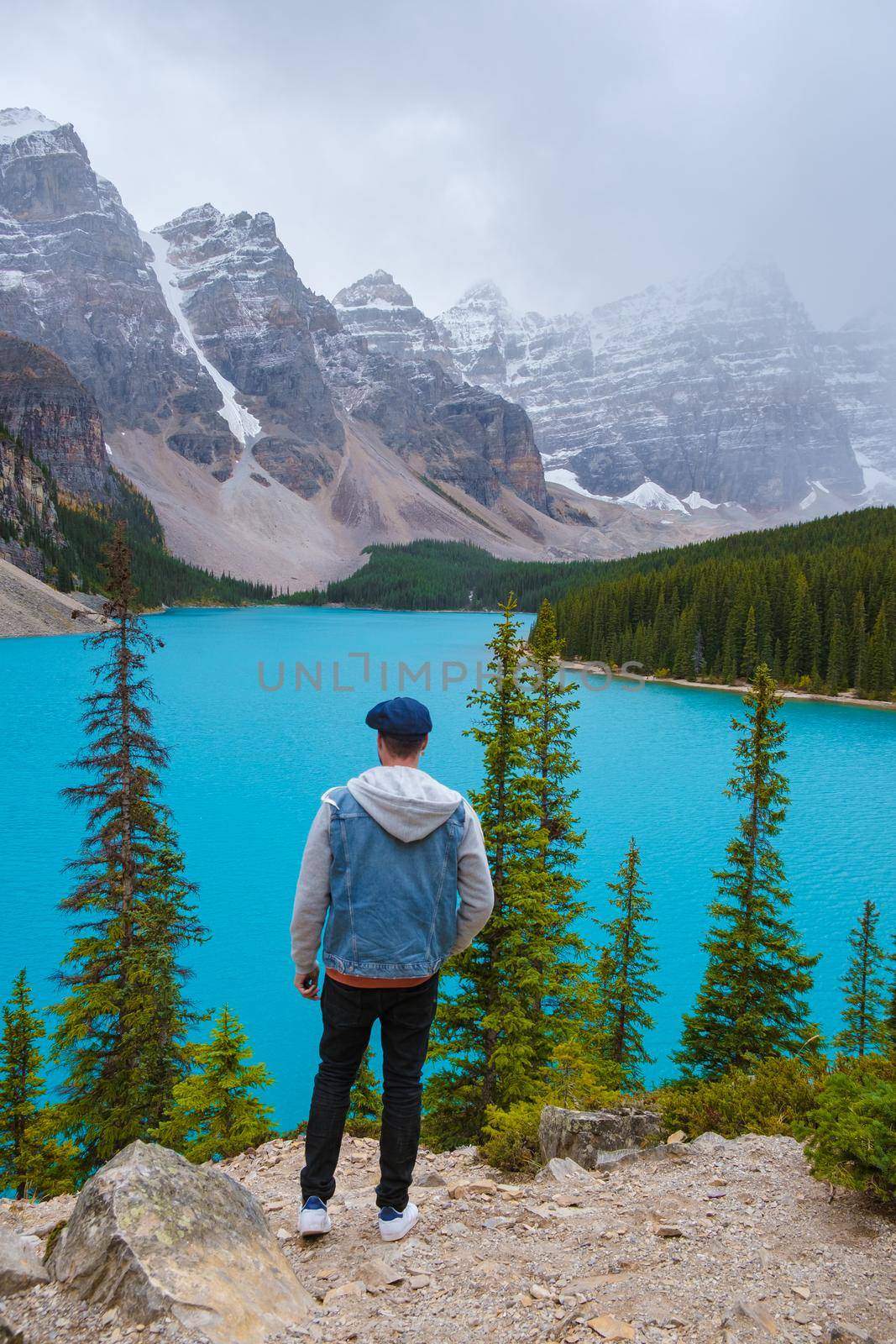 Lake moraine during a cold snowy day in Autumn in Canada, Beautiful turquoise waters of the Moraine lake with snow. Banff National Park of Canada Canadian Rockies, young men standing by the lake