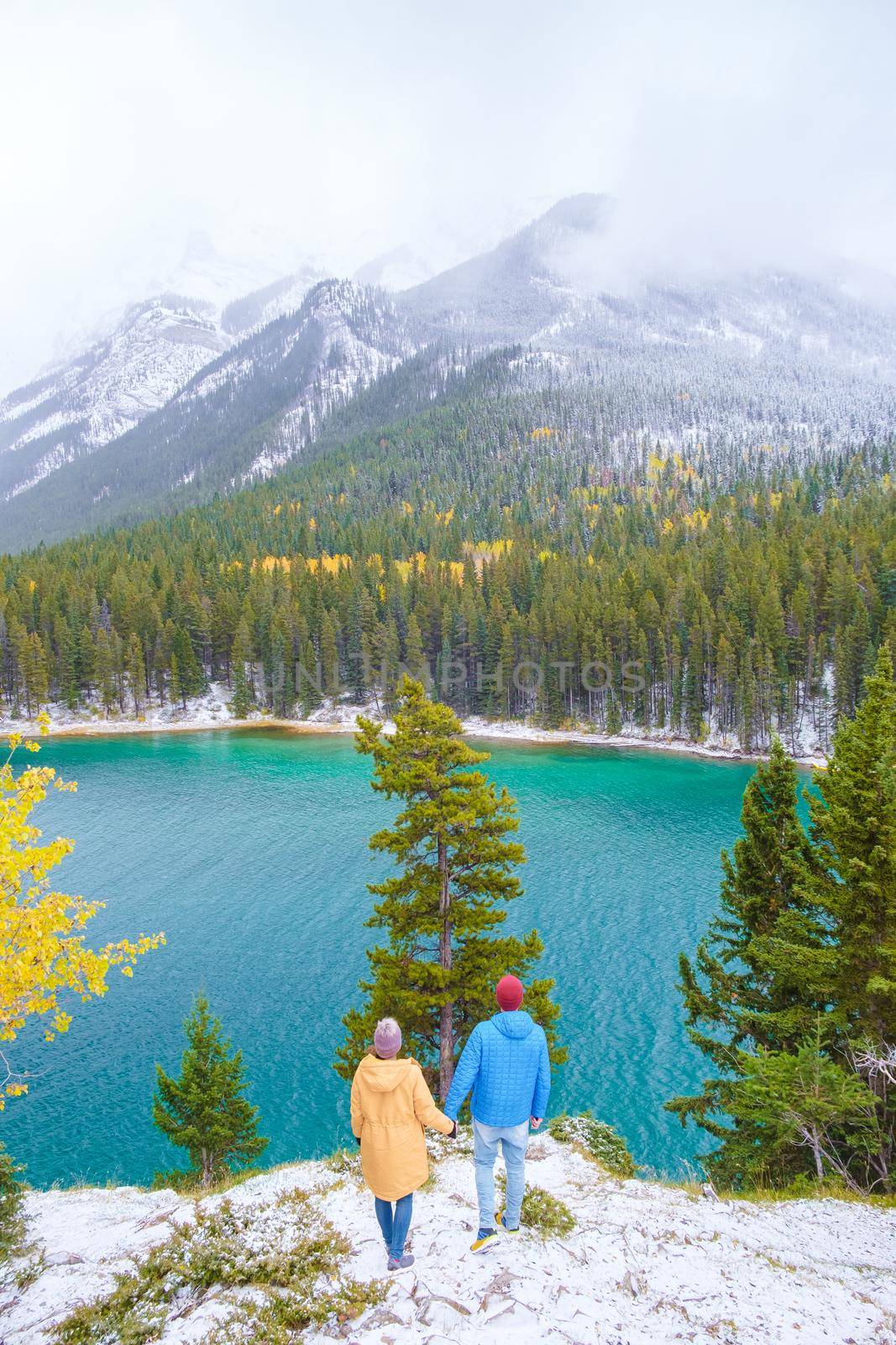 Minnewanka lake in the Canadian Rockies in Banff Alberta Canada with turquoise water, Lake Two Jack in the Rocky Mountains of Canada. a couple of men and women hiking by the lake during snow weather