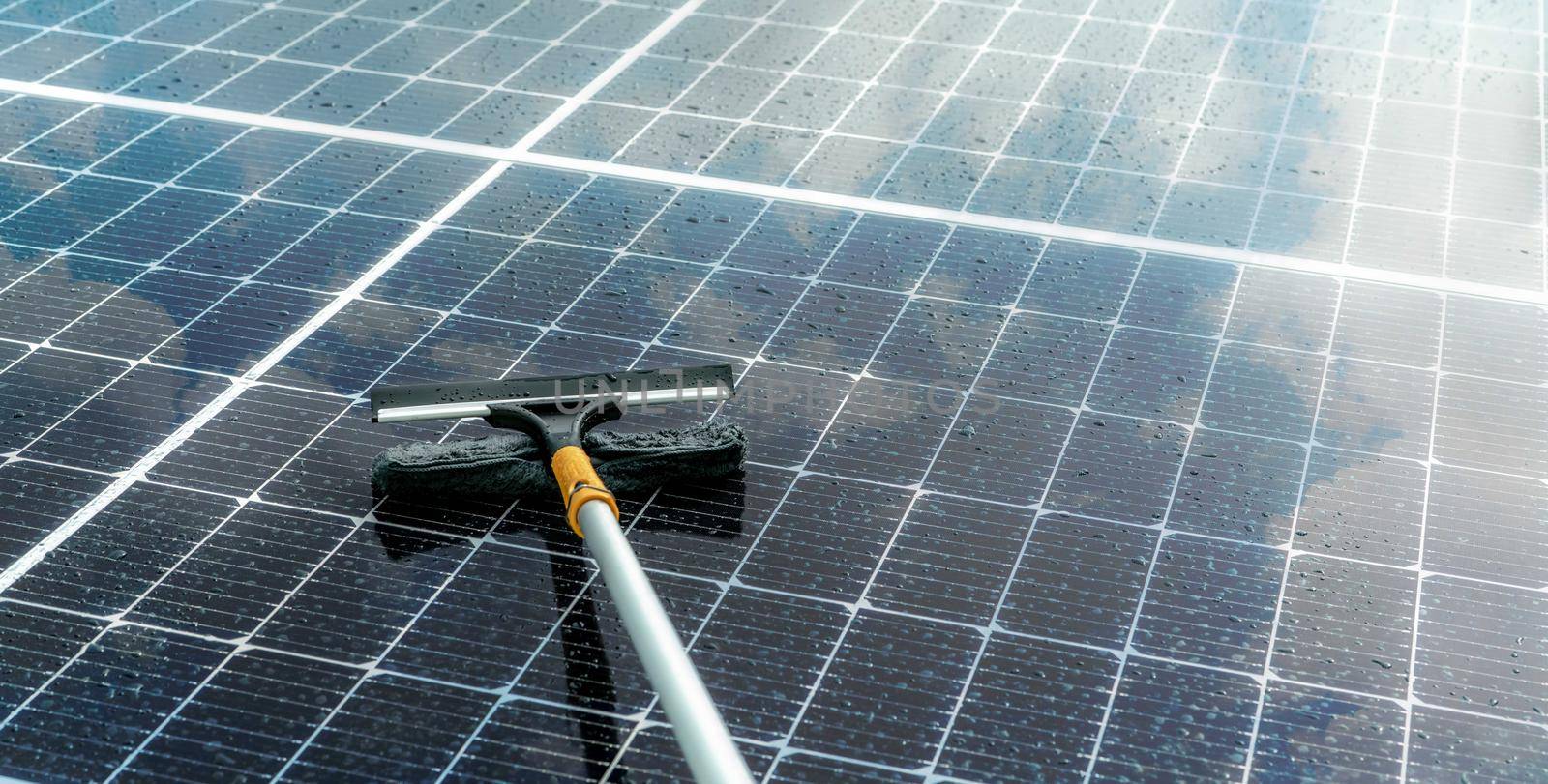 Cleaning solar panel with microfiber mop on wet roof. Solar panel or photovoltaic module maintenance service. Sustainable resource. Solar power. Green energy. Sustainable development technology.