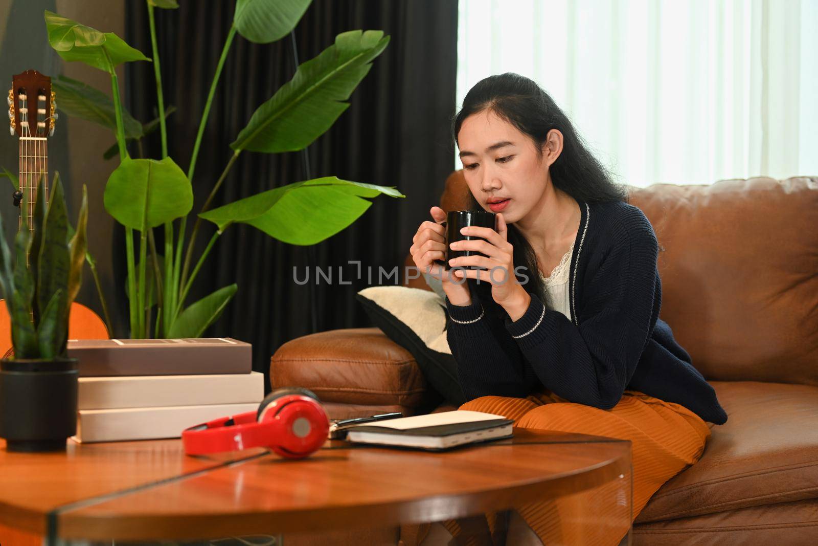 Pleasant young woman drinking hot coffee and relaxing on couch, enjoying stress free peaceful mood in an autumn day.