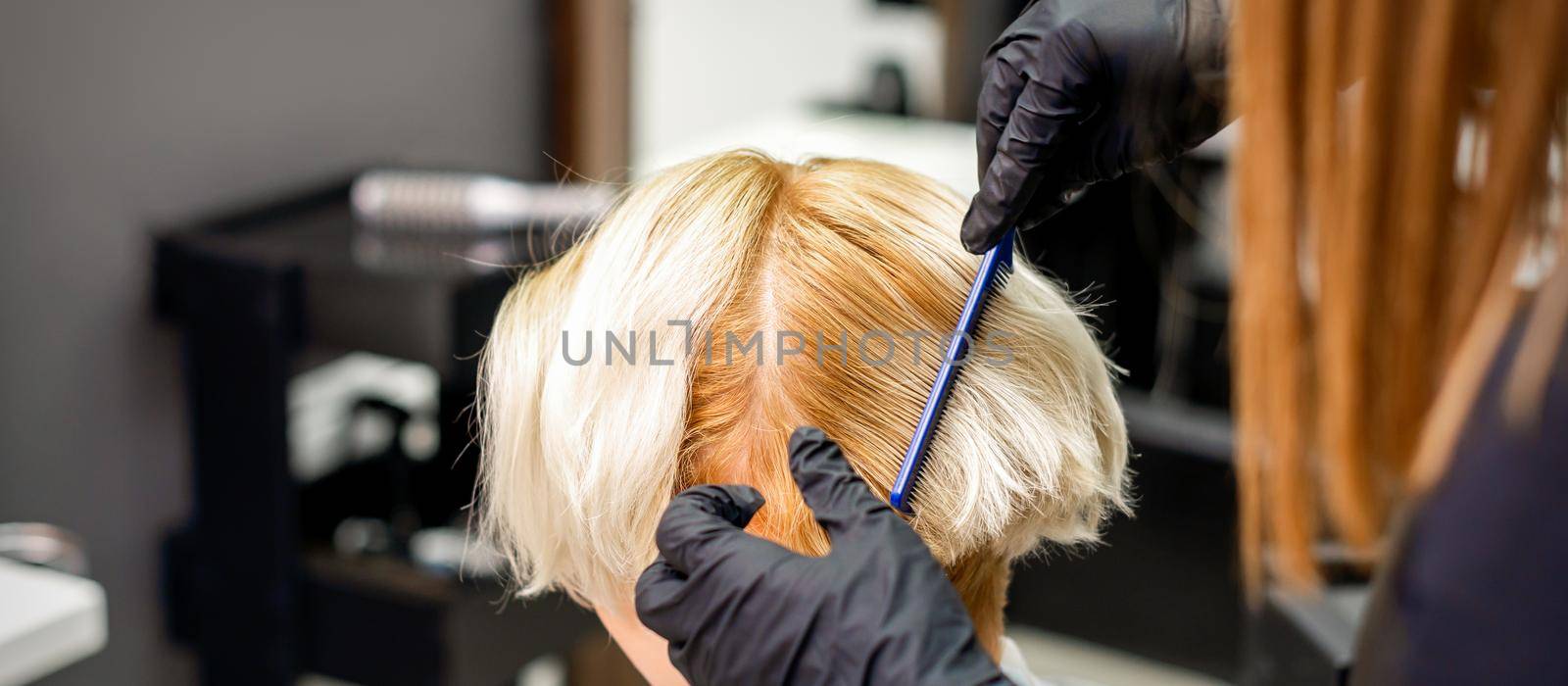 Hairdresser combing female short blonde hair before dyeing in a hair salon