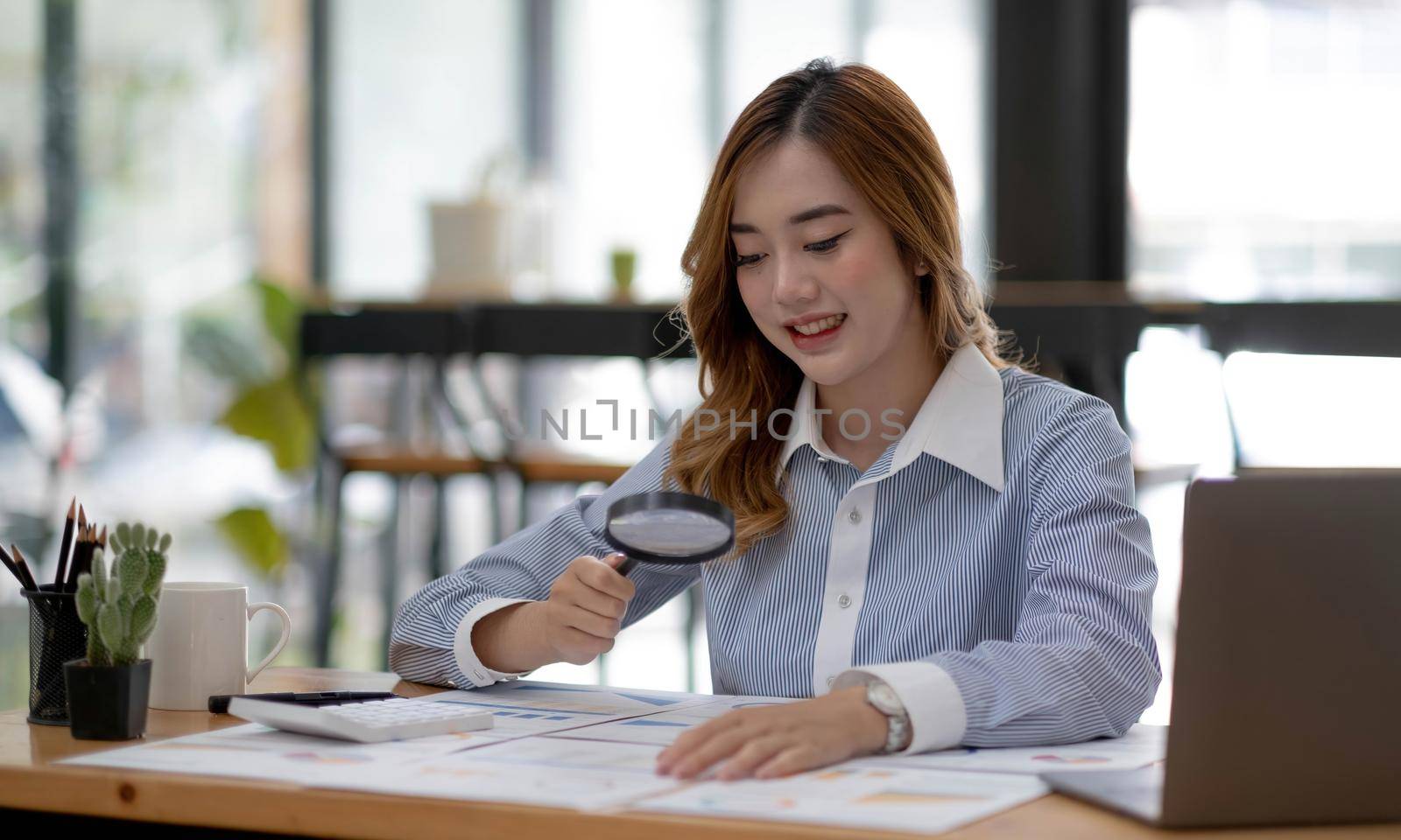 Close up of businesswomen holding magnifying glass finding a wooden shape of a house, realtor, agent, insurance, developer, planning