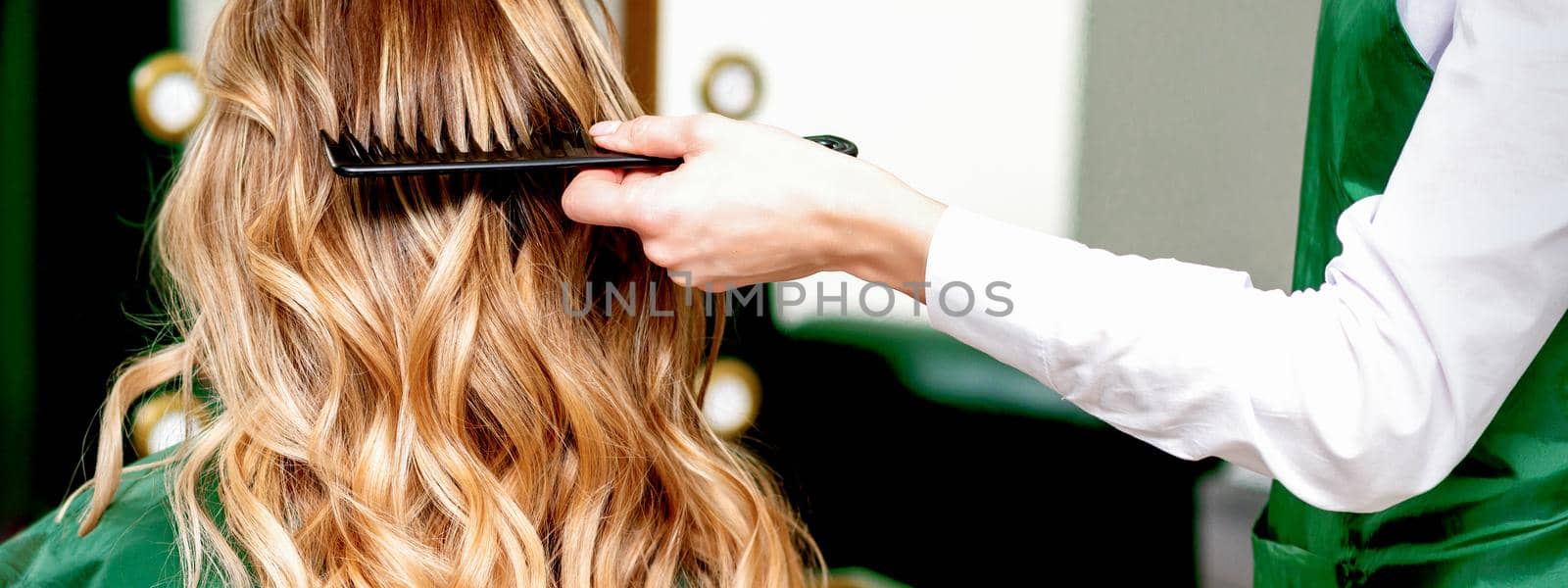 Hairdresser combing wavy hair of woman by okskukuruza