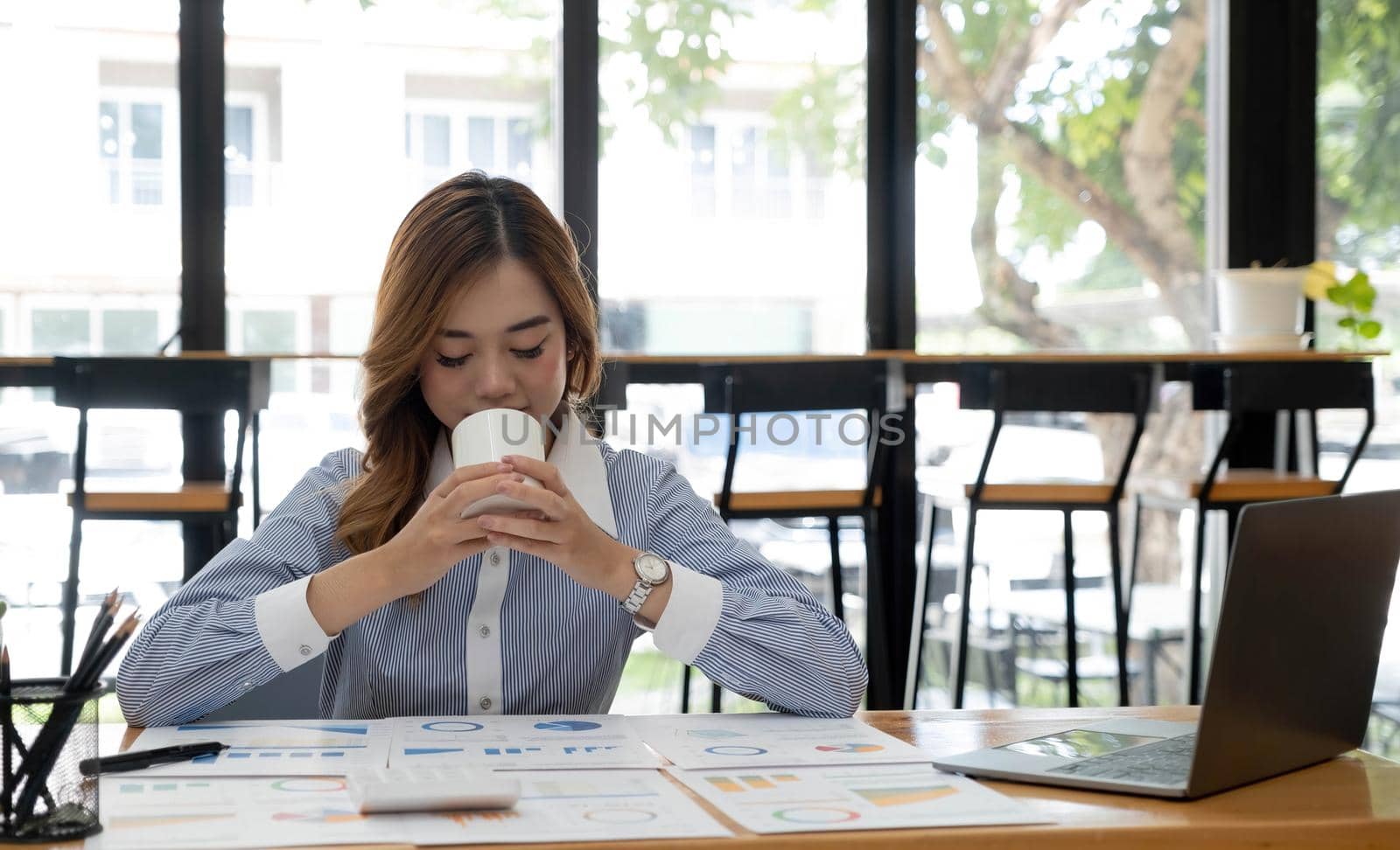 Beautiful young Asian businesswoman smiling holding a coffee mug and laptop working at the office..