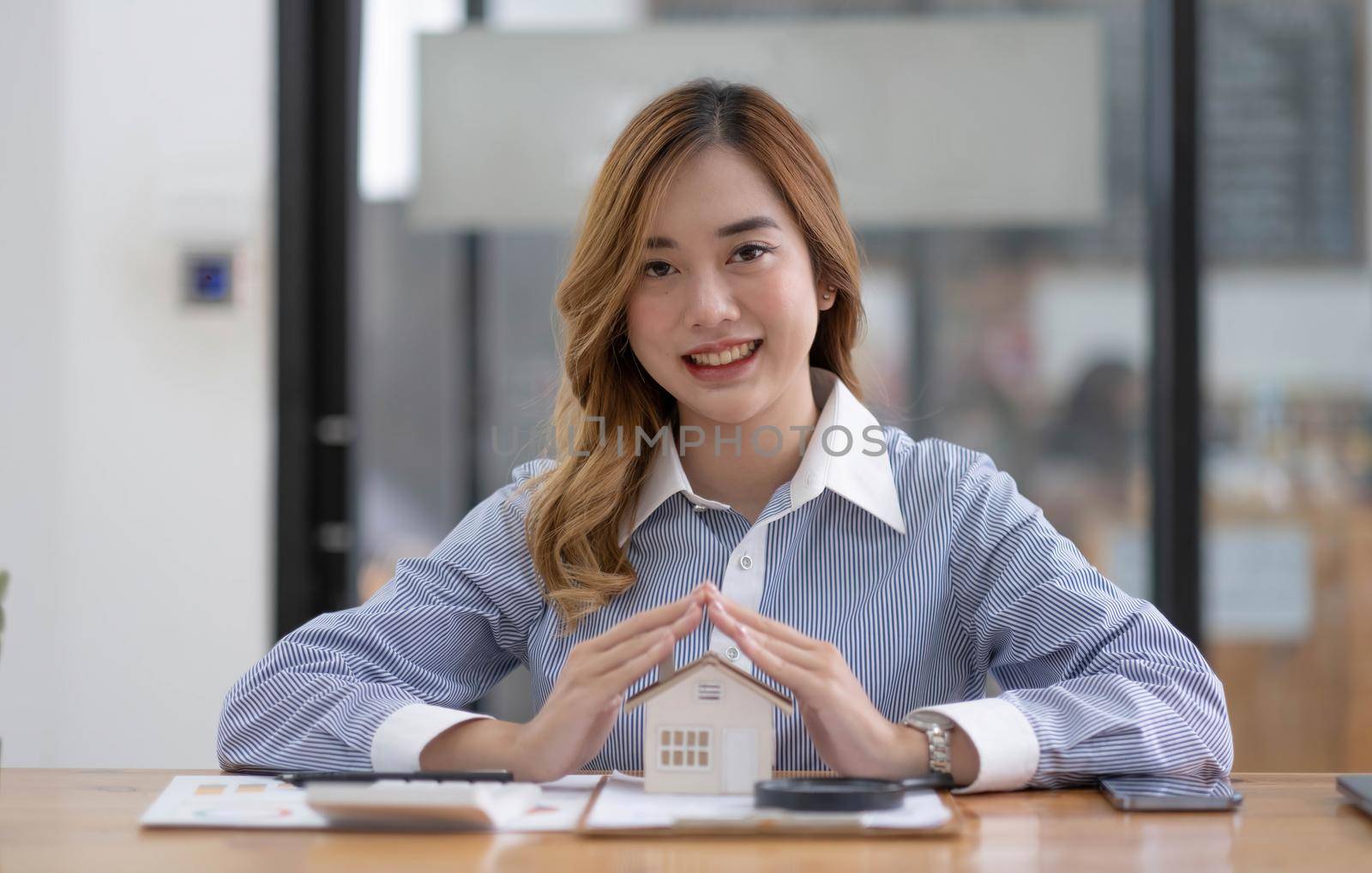 Miniature house in the hands of an Asian woman real estate agent home loan working at the office. Looking at the camera..