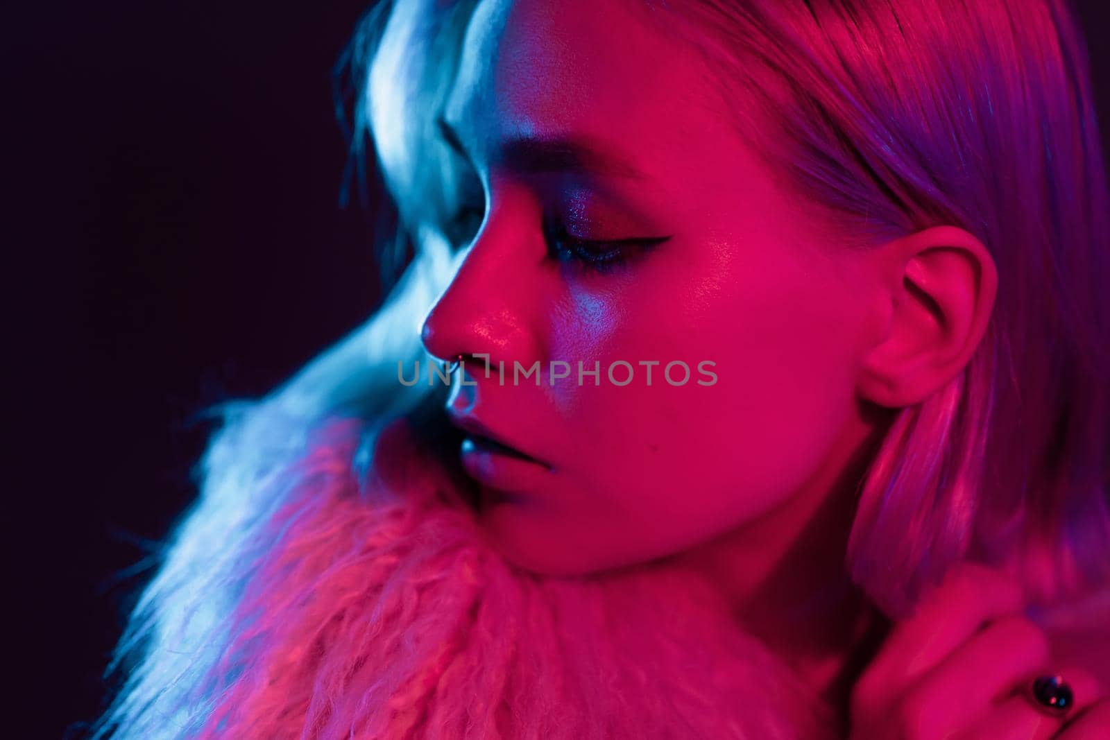 Close up portrait of millennial pretty fashion girl in fluffy fur coat in pink neon light. Dyed blue hair. Mysterious hipster teenager concept