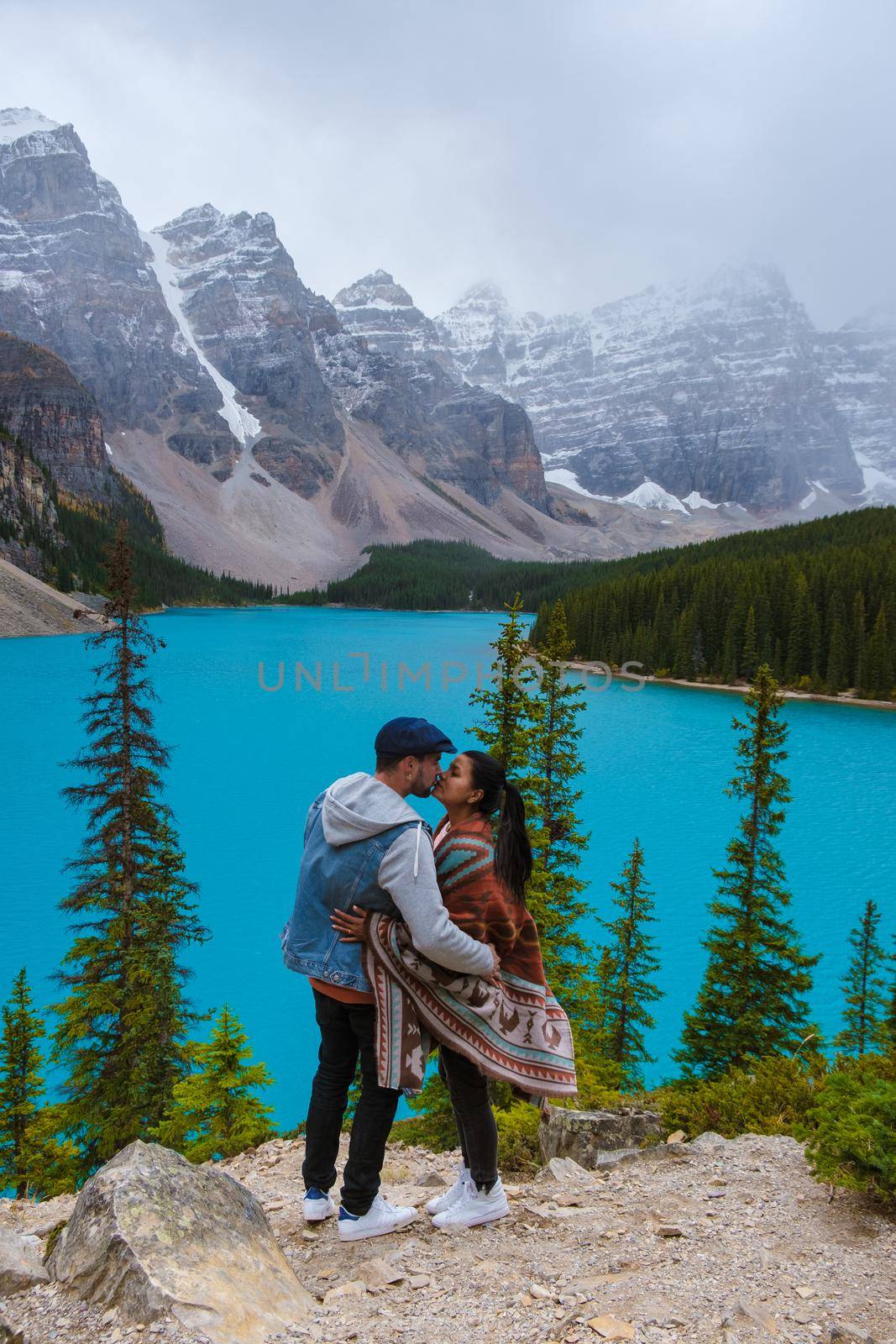 Lake moraine during a cold snowy day in Canada, turquoise waters of the Moraine lake with snow. Banff National Park of Canada Canadian Rockies. Young couple men and women standing by the lake