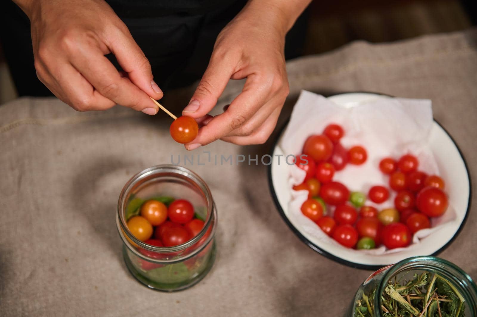 Overhead view of chef's hands putting fresh organic home grown cherry tomato in sterilized jar, while canning delicacy for organic seasonal vegetables for winter. Preserving food. Pickling. Marinating
