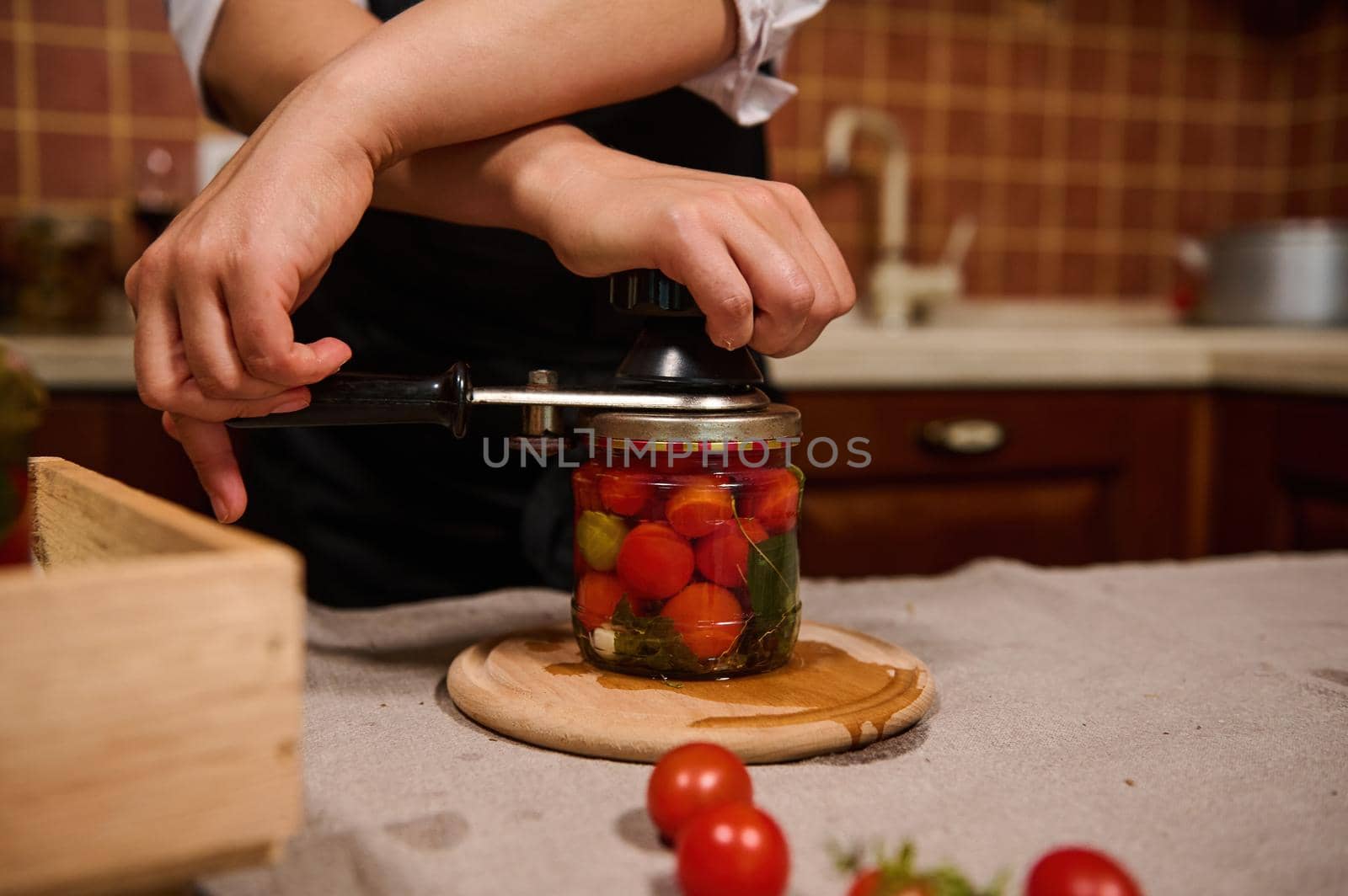 Process of preserving cherry tomatoes for the winter. Women's hands close the lids of jars with ripe red juicy organic tomatoes with a special key. Canning food according traditional family recipe