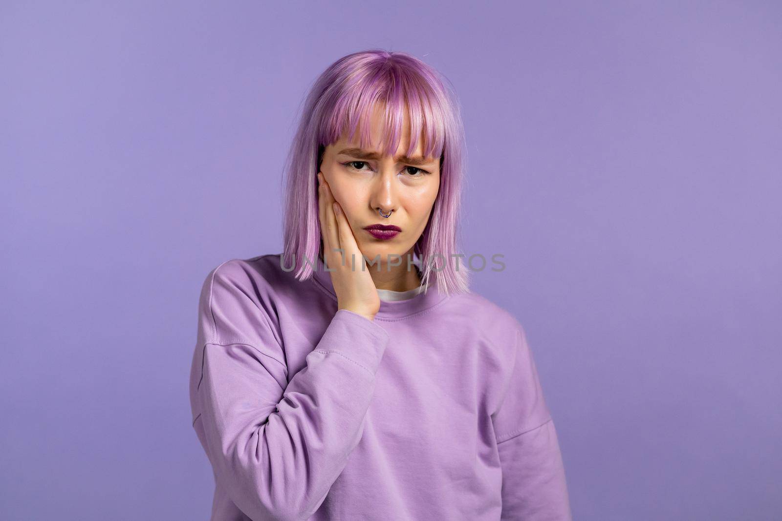 Young woman with dyed purple hair have tooth pain on violet studio background. Toothache, dental problems, stomatology and medicine concept. High quality photo