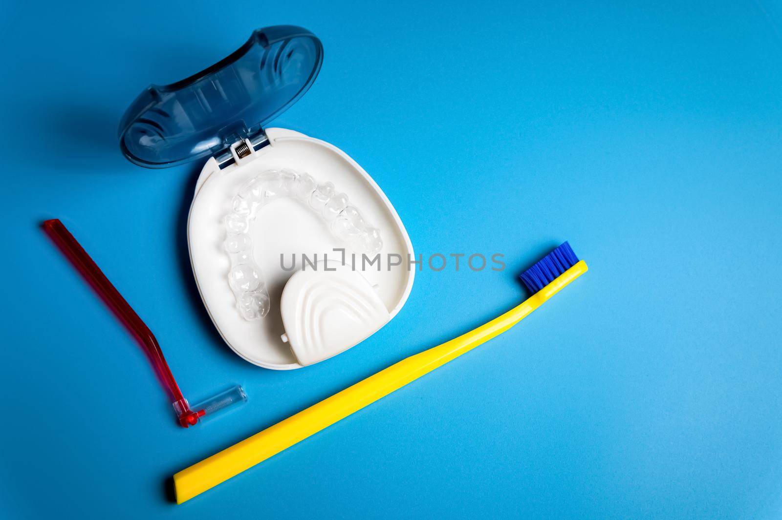 Invisible dental braces for teeth, transparent teeth aligners, plastic braces, retainers for straightening teeth, toothbrush and interdental brush on blue background, top view.