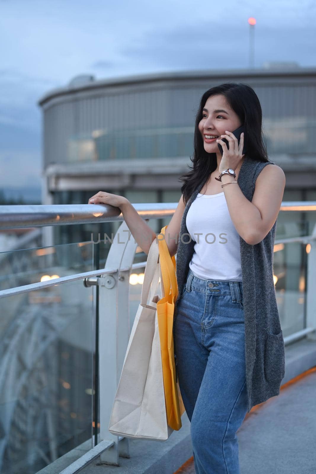 Attractive asian woman with shopping bags standing on terrace of modern building overlooking the city. Lifestyle concept by prathanchorruangsak