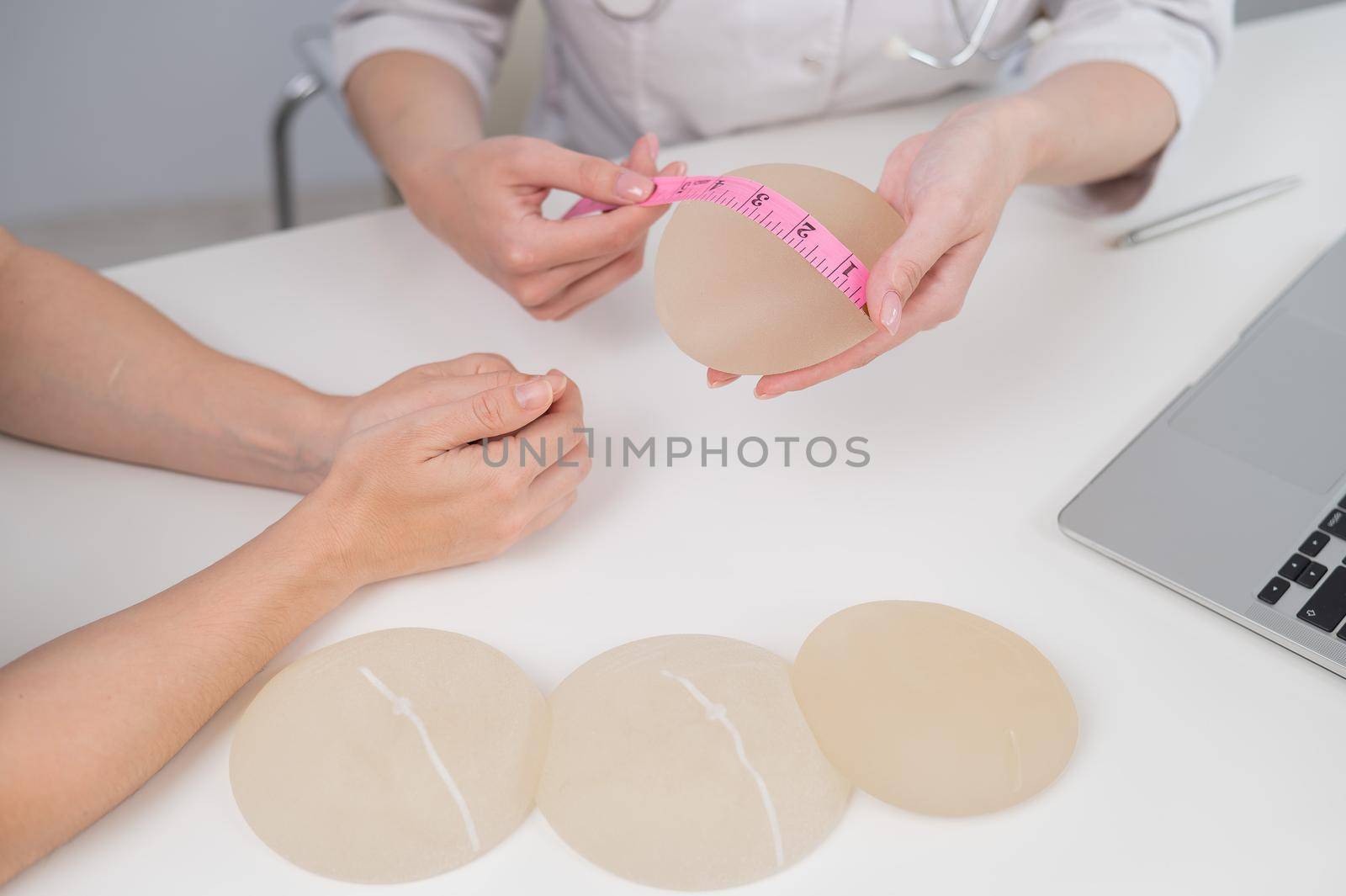 A plastic surgeon measures breast implants with a centimeter tape and demonstrates to a female patient. by mrwed54