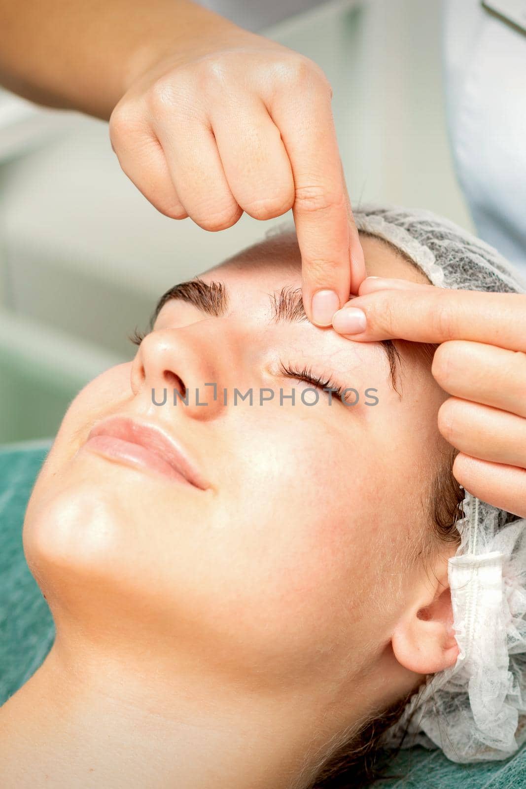 Beautician's hands make massage on eyebrow for a woman while a facial massage in cosmetology clinic center