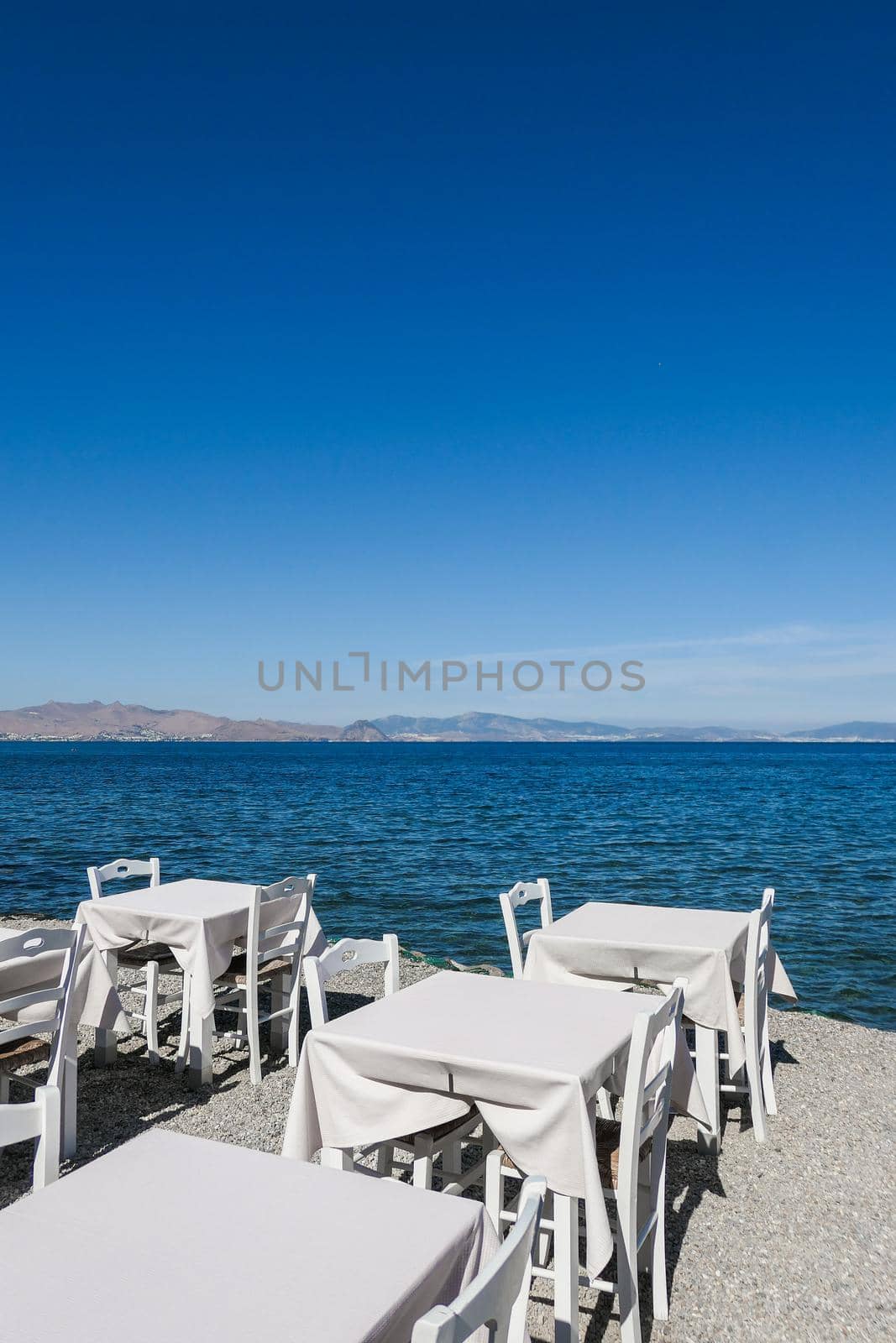 White restaurant tables on the beach in summer - travel, vacation and summer concept. The perfect lunch with a sea view