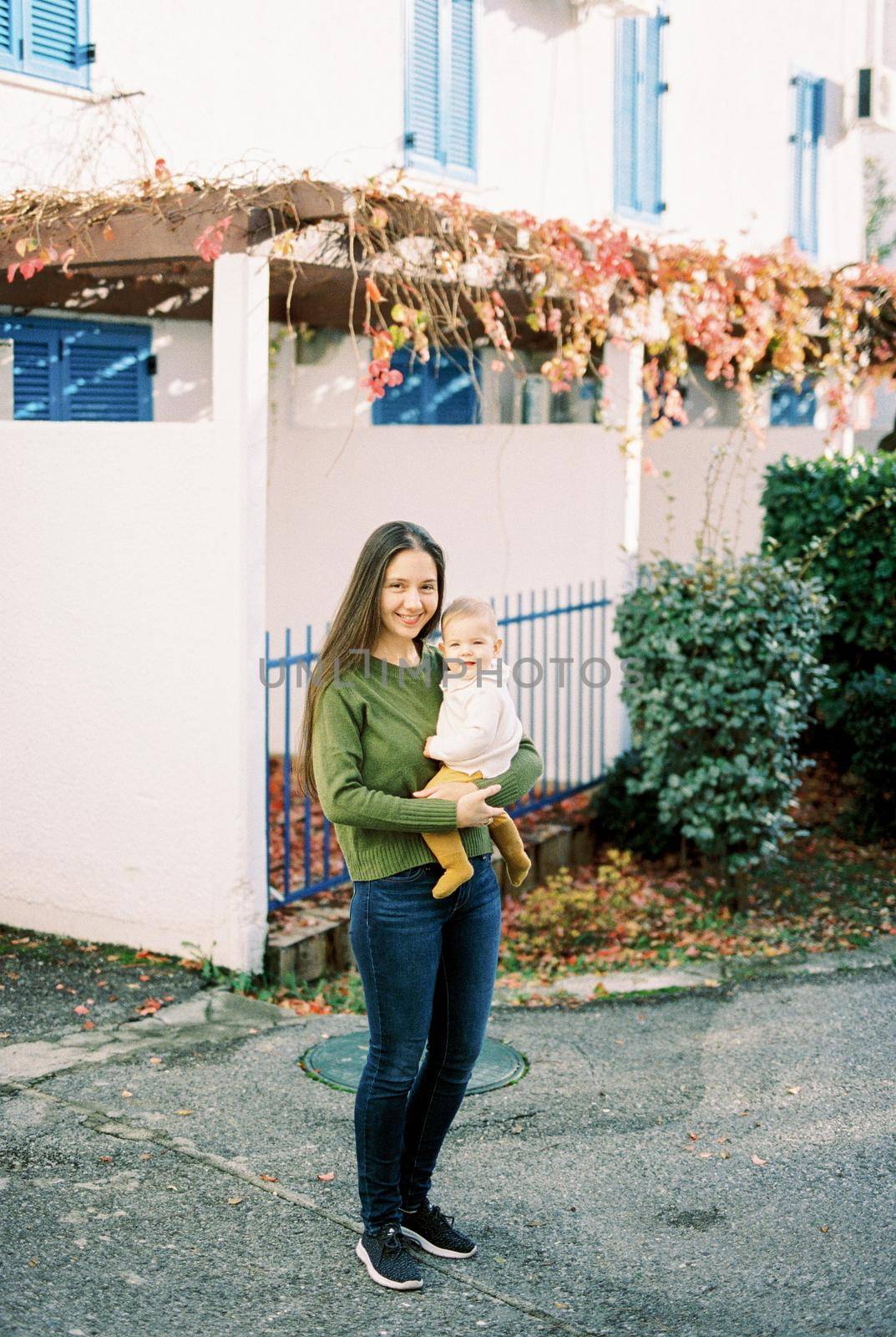 Mom with a baby in her arms stands in the yard near the house. High quality photo