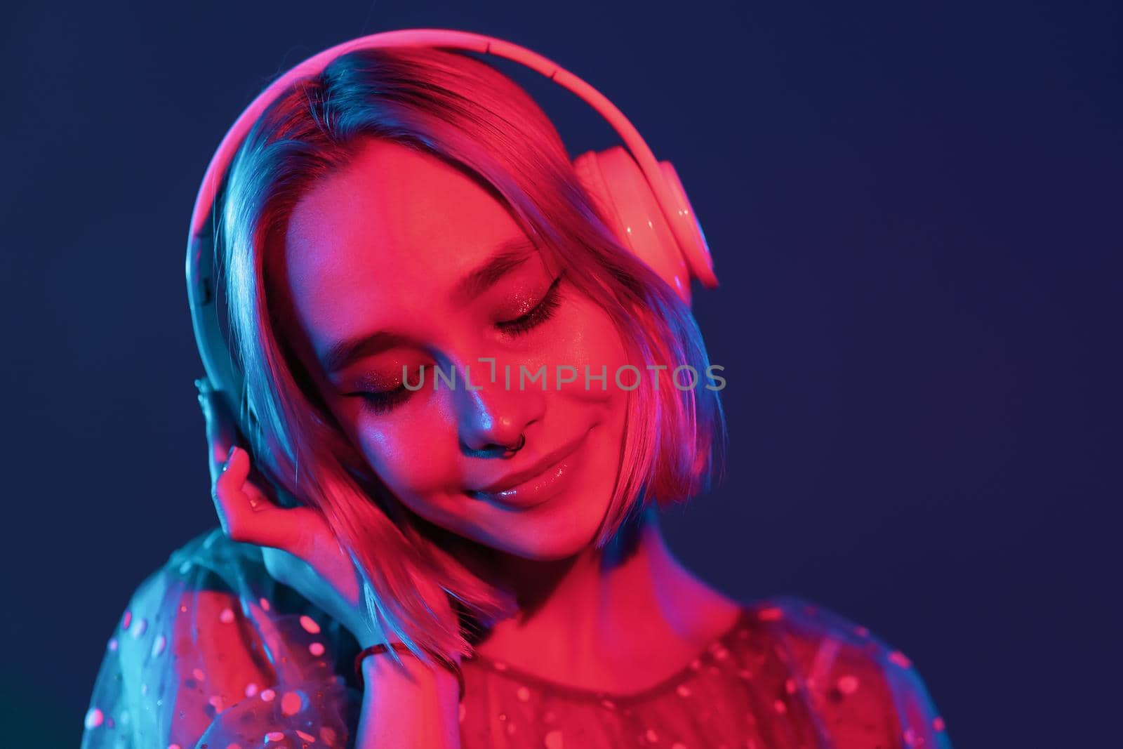 Mysterious hipster teenager listening to music with headphones. Portrait of millennial pretty girl with short hairstyle with neon light. Dyed blue and pink hair
