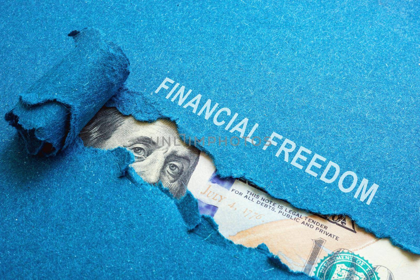 The inscription financial freedom on torn paper and dollars under it. by designer491