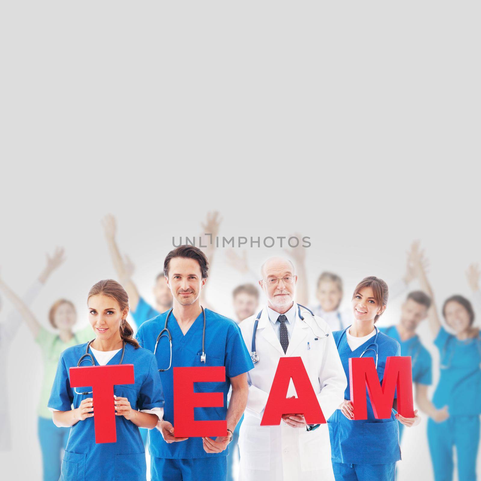 Group portrait of happy medical doctors workers holding TEAM letters on gray background, blue uniform