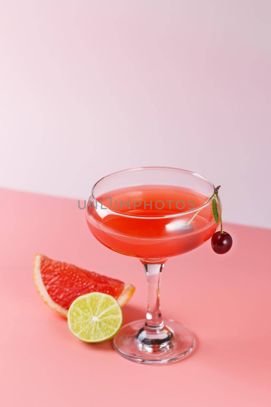 Fresh grapefruit juice in a glass with grapefruit slices, lime and cherry on a pink background. Copy spase
