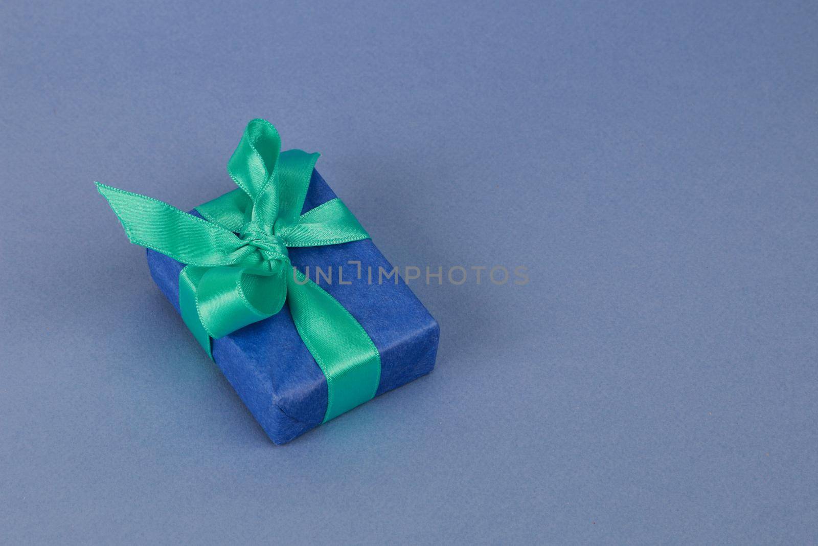 A blue gift box with a green ribbon on a blue paper background. by gelog67