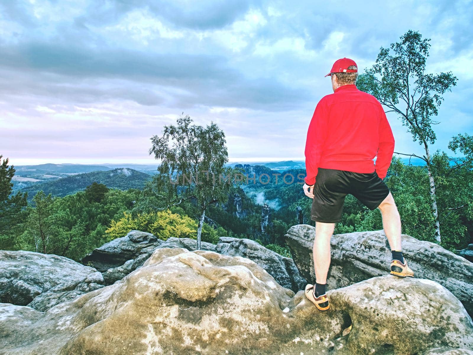 Runner in pink jacket and light black shorts. Short ginger hair man on the path in rocky mountains.