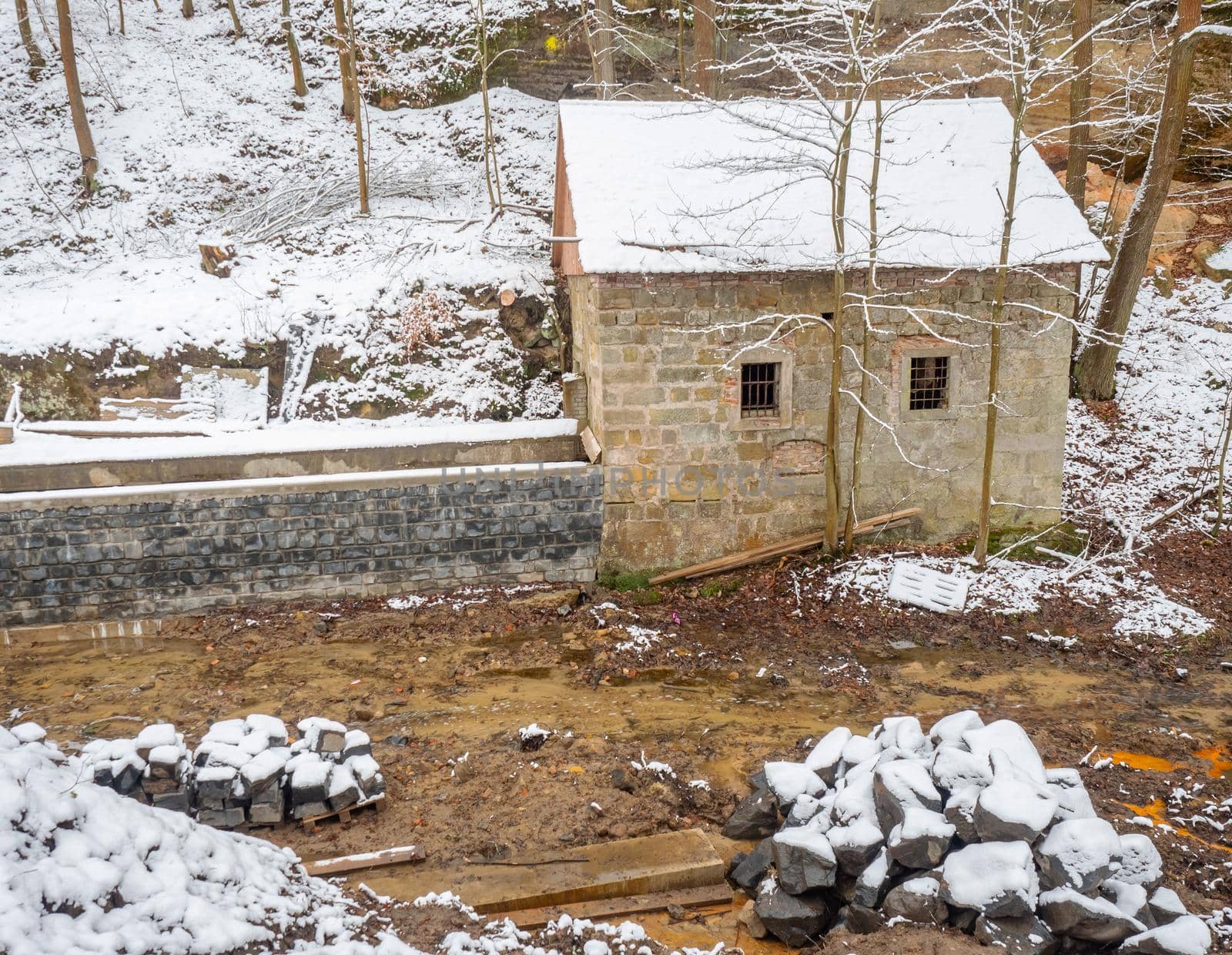 Historical building of water power plant at dam during renewal period. Snowy winter forest.