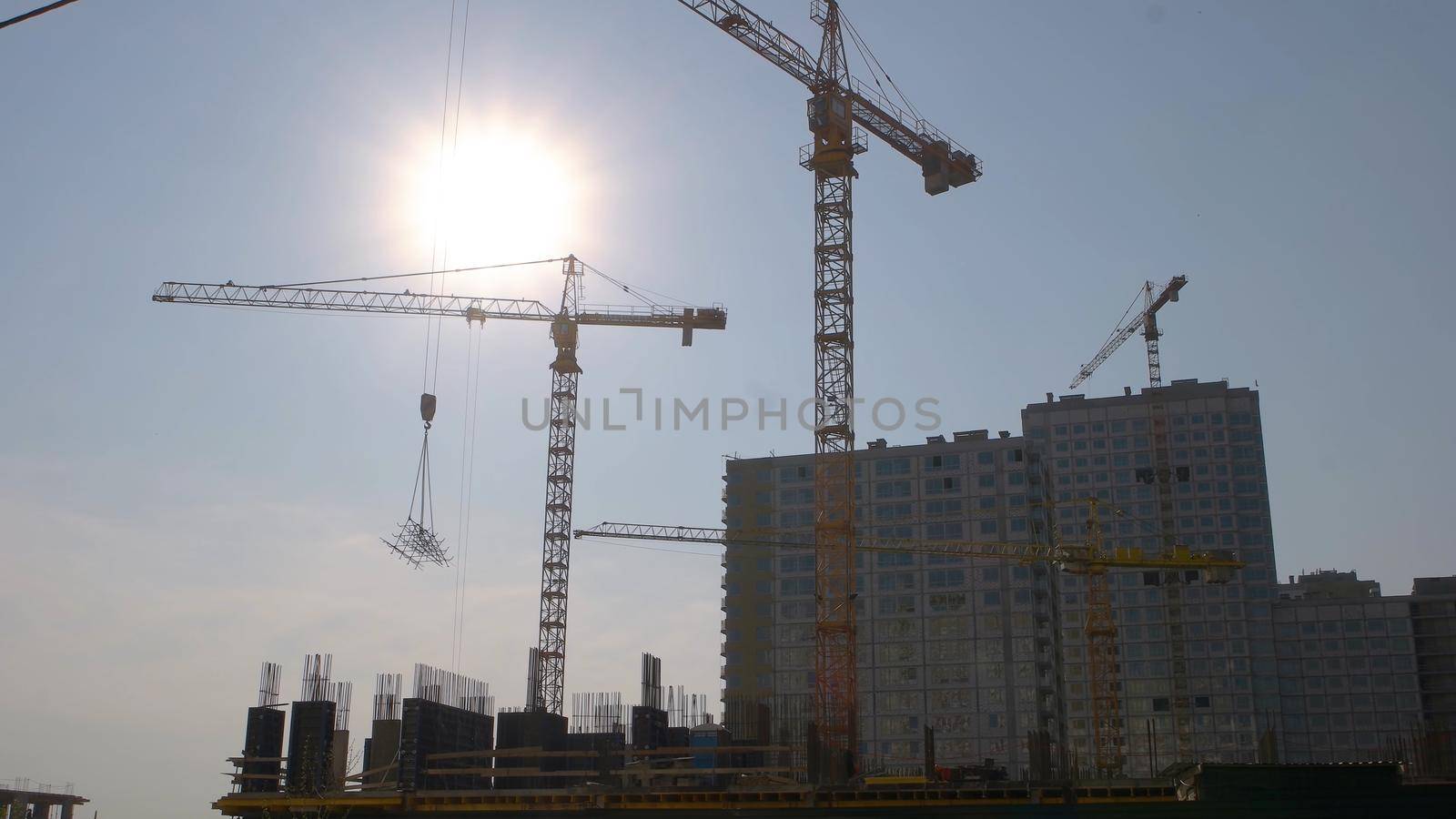 Yellow crane carrying a metal frame on the construction. Blue sky with a brigh sun. Fast speed motion.