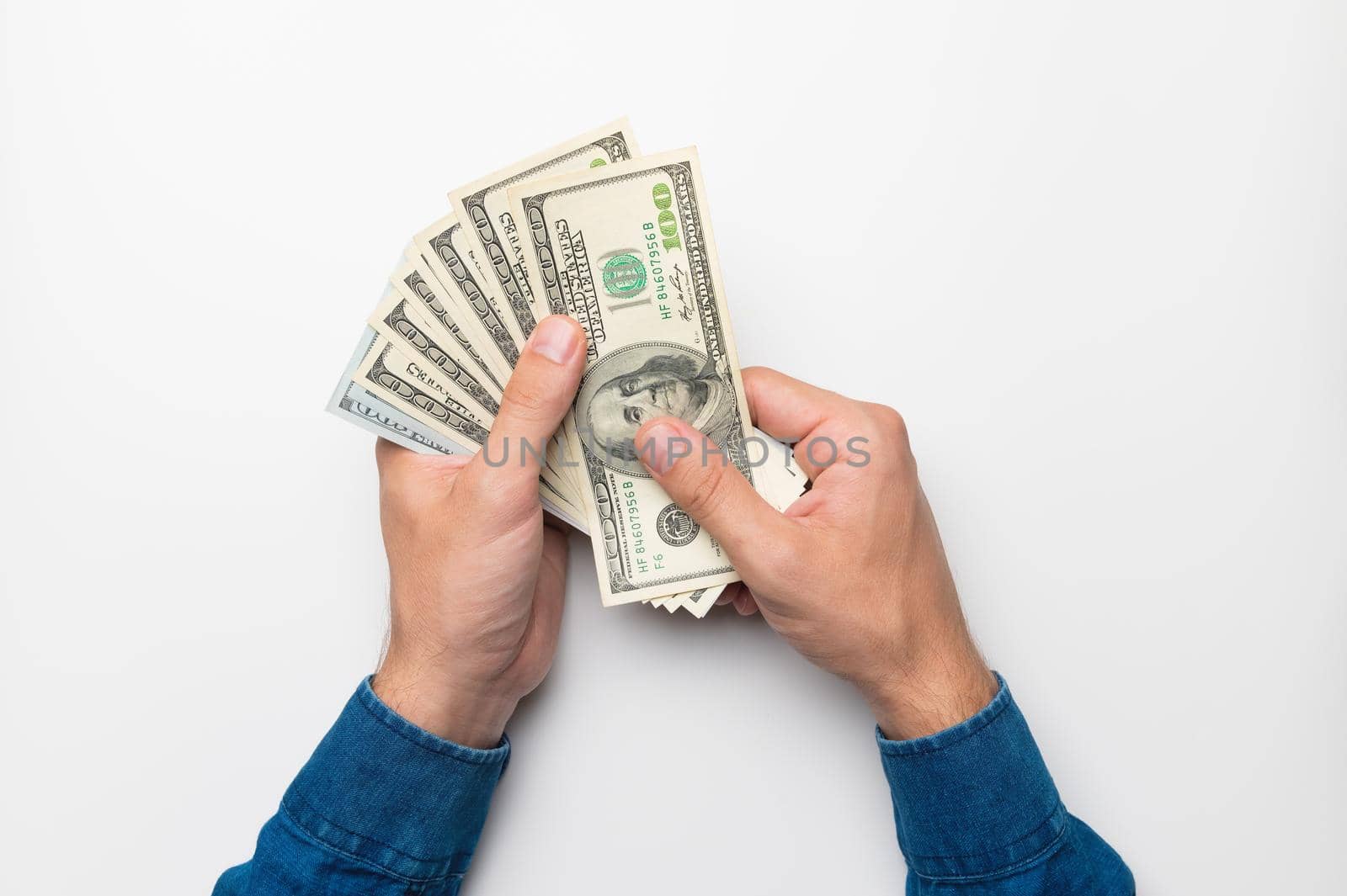 A first-person photograph showing male hands holding a fan of one hundred dollar bills against a white background. studio shot.