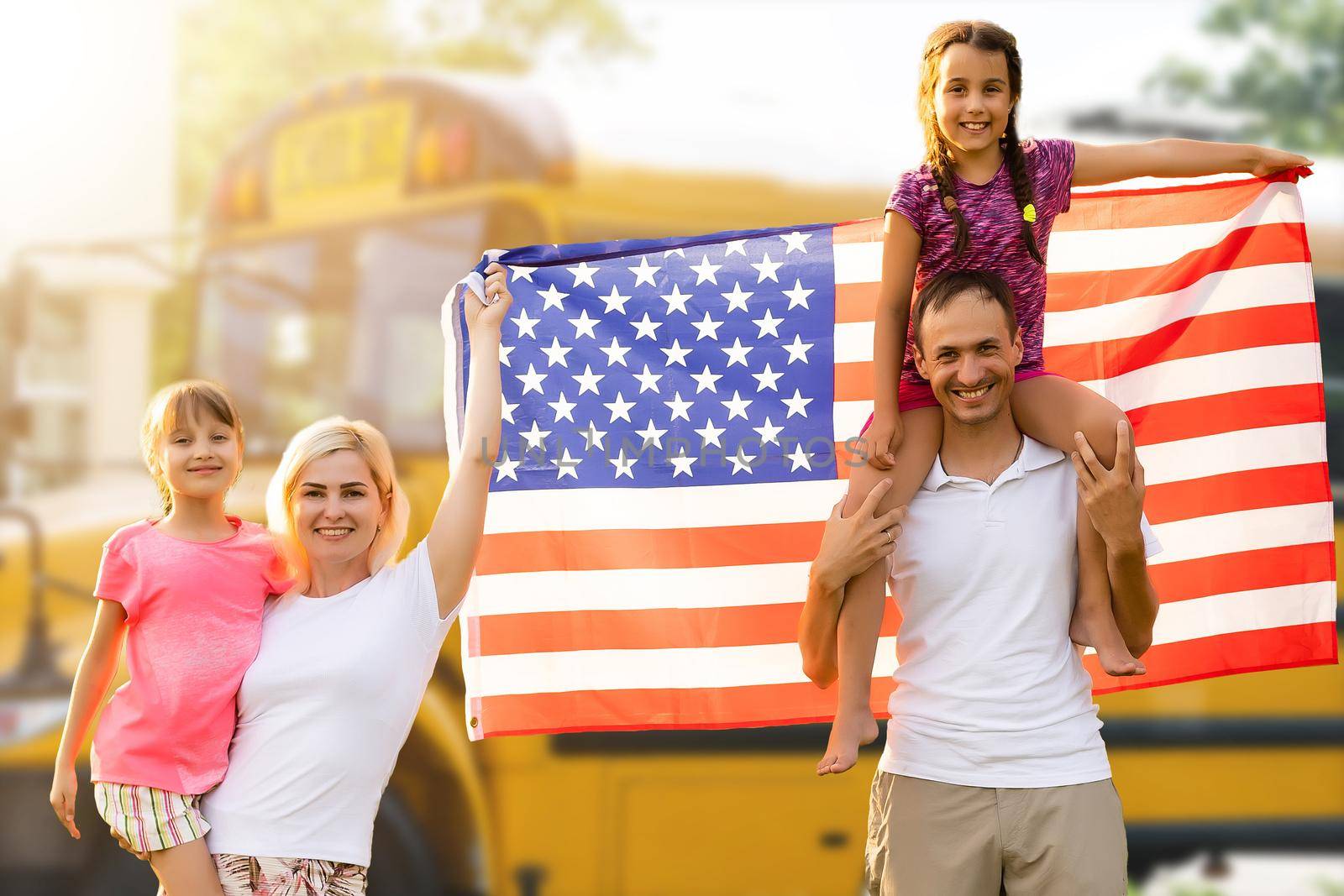Happy young family with national flags of USA near the school bus.