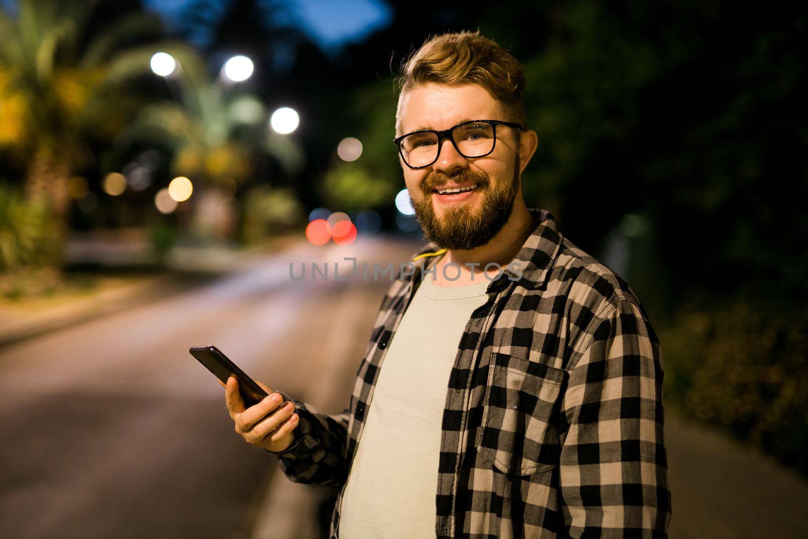 Man waits taxi by using transportation app on night street. Technologies and city
