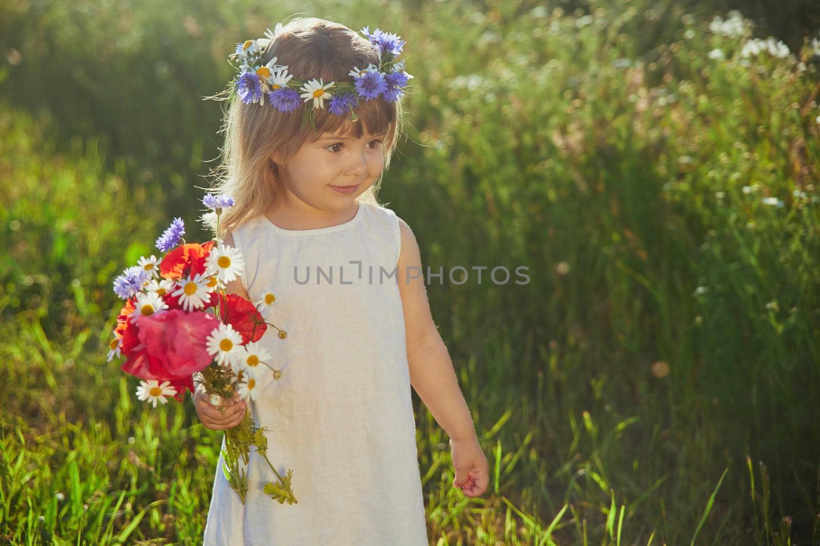 charming child in linen dress walks in a field with flowers at sunset