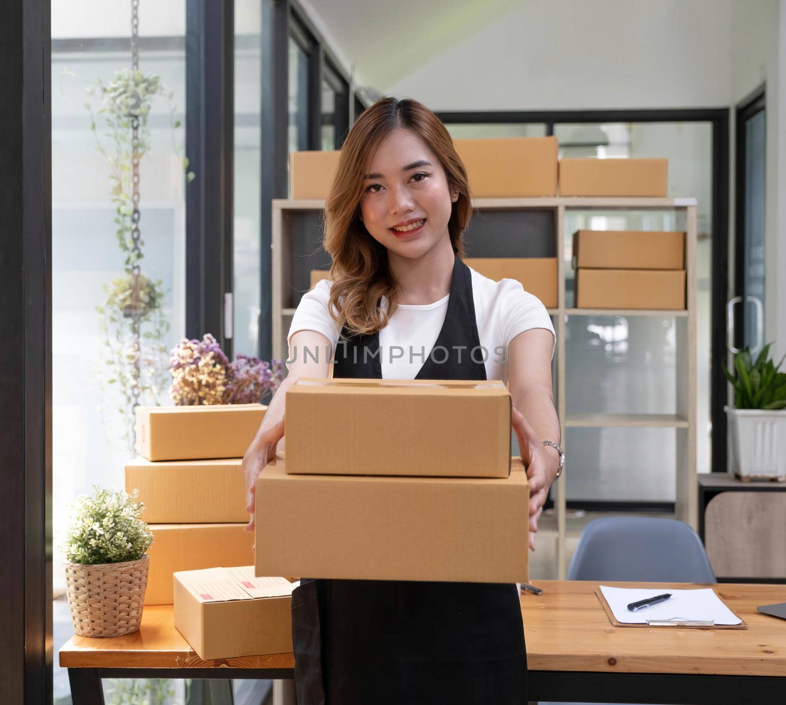 Startup SME small business entrepreneur SME or freelance Asian woman using a laptop with box, Young success Asian woman with her hand lift up, online marketing packaging box and delivery, SME concept. by wichayada